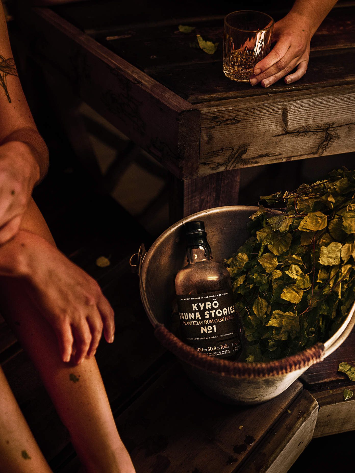 Kyrö Sauna Stories No.1 whisky bottle resting in a birch whisk bowl inside a dimly lit sauna.