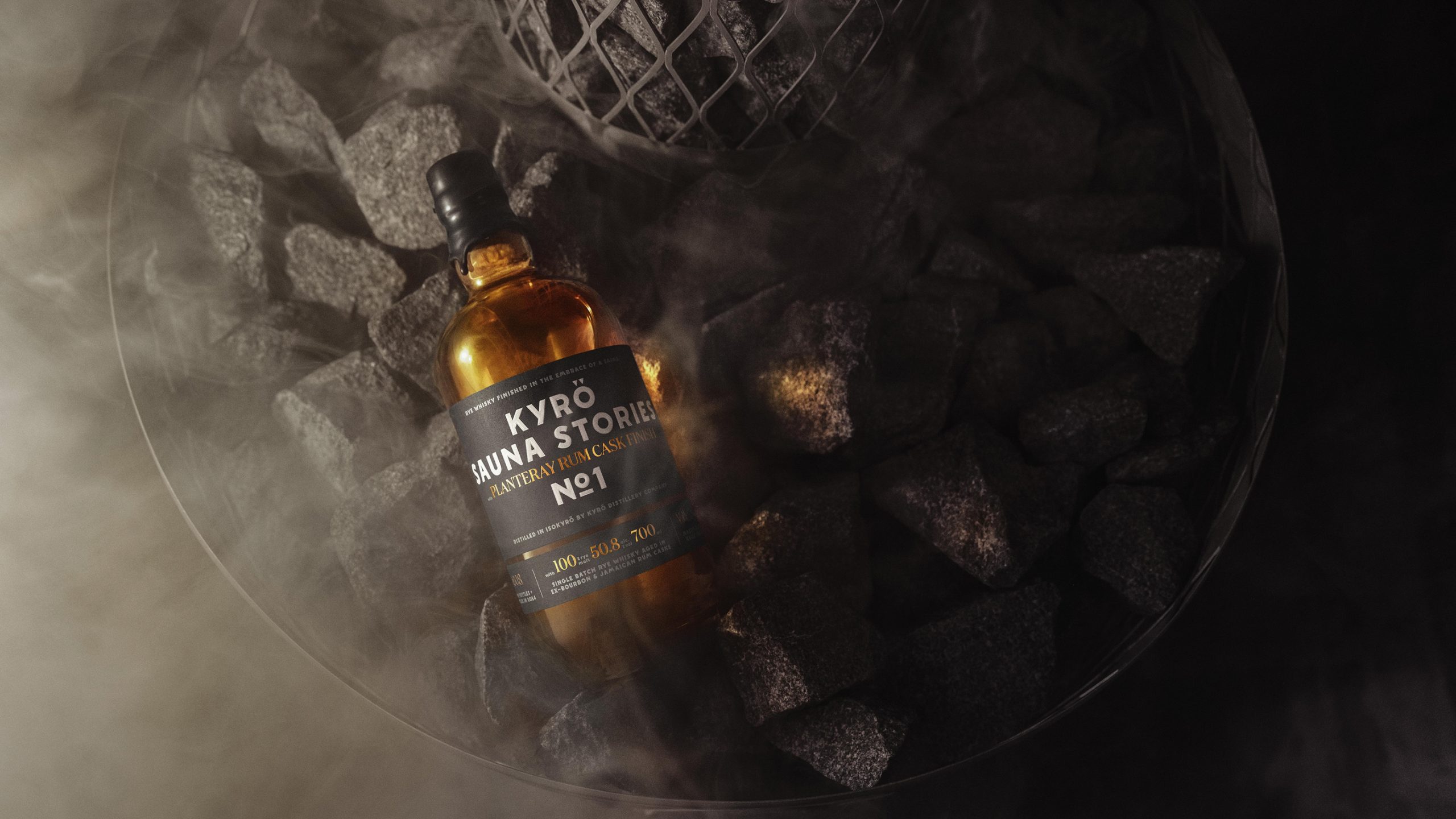 Kyrö Sauna Stories No.1 rye whisky bottle resting on dark sauna stones with steam rising around it.