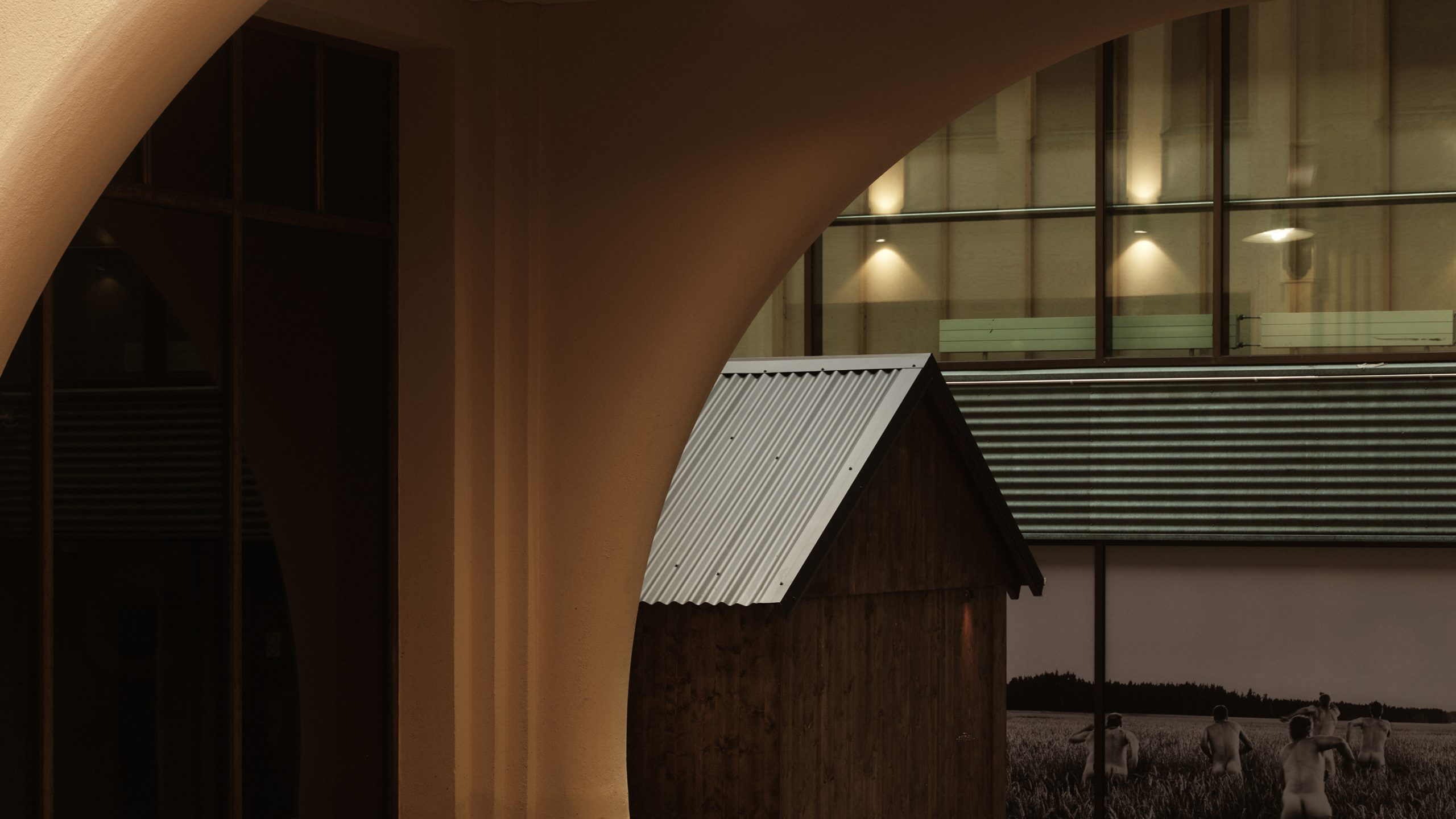 Kyrö Distillery interior with warm-lit arch, rustic wooden shed with corrugated metal roof, and large industrial windows.