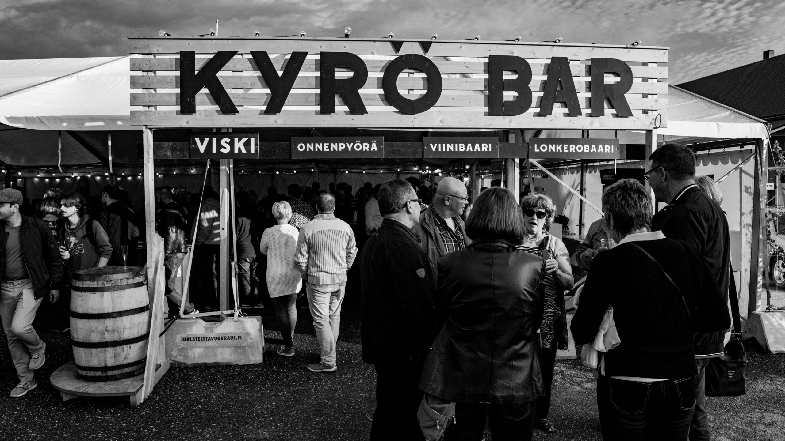 Kyrö Bar tent at an outdoor event, featuring a wooden sign with sections for viski, viinibaari, and lonkerobaari.