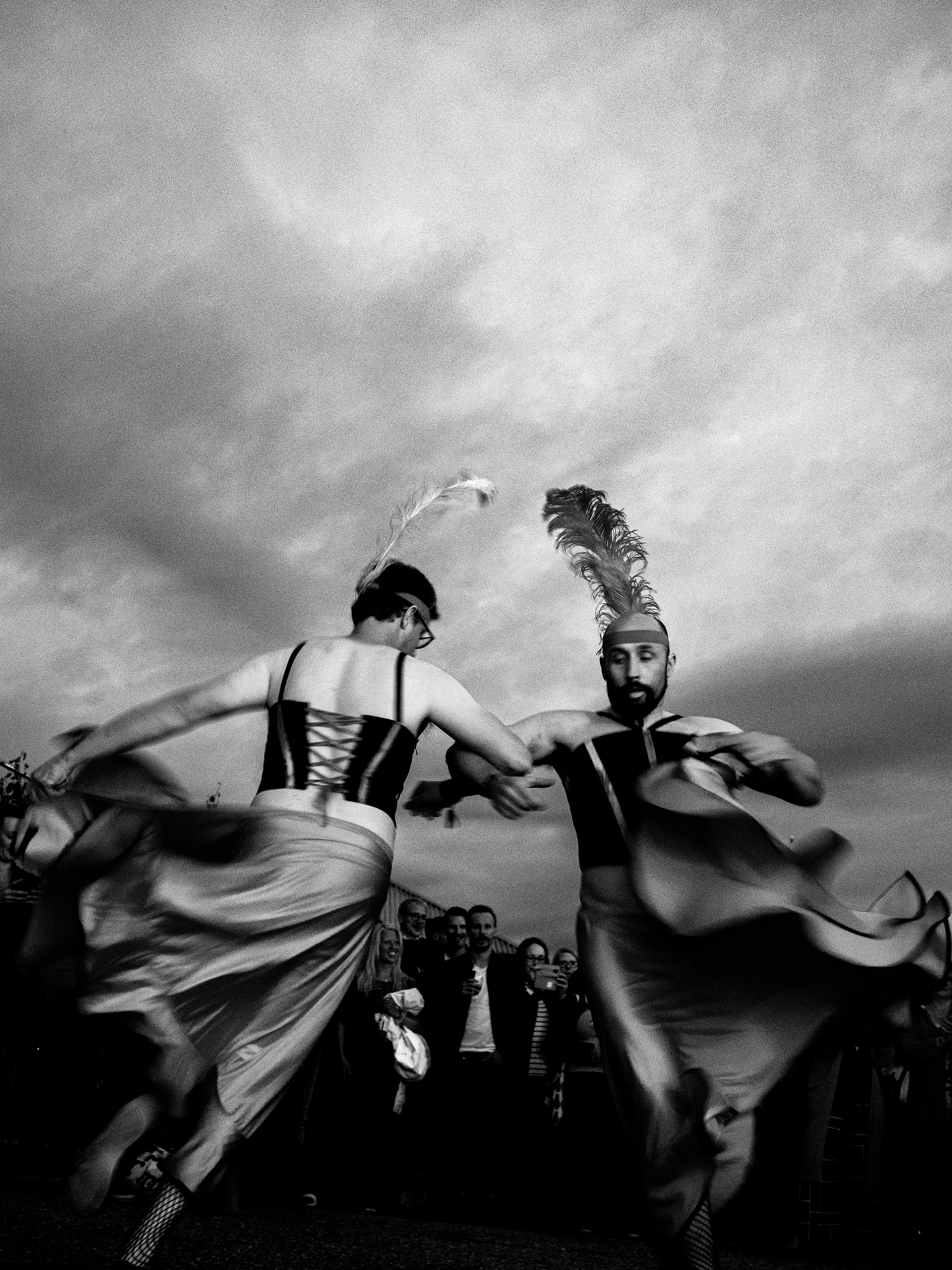 Two performers in feathered headdresses and flowing skirts dance energetically outdoors at a Kyrö Distillery event.
