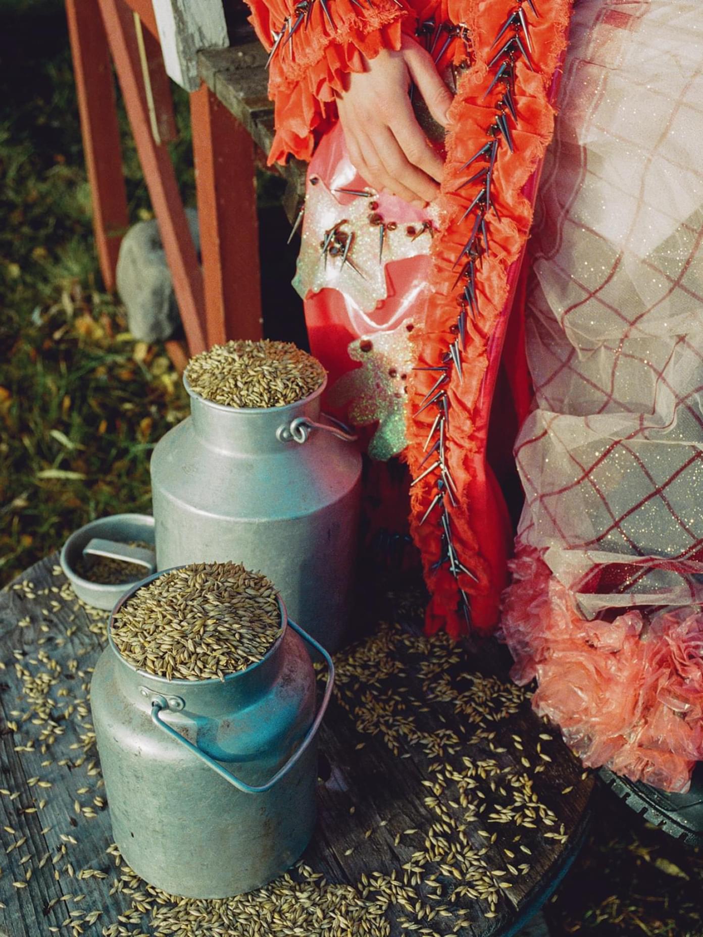 Mö branding: vintage milk churns filled with grain beside a figure in an ornate orange ruffled costume with spike details.
