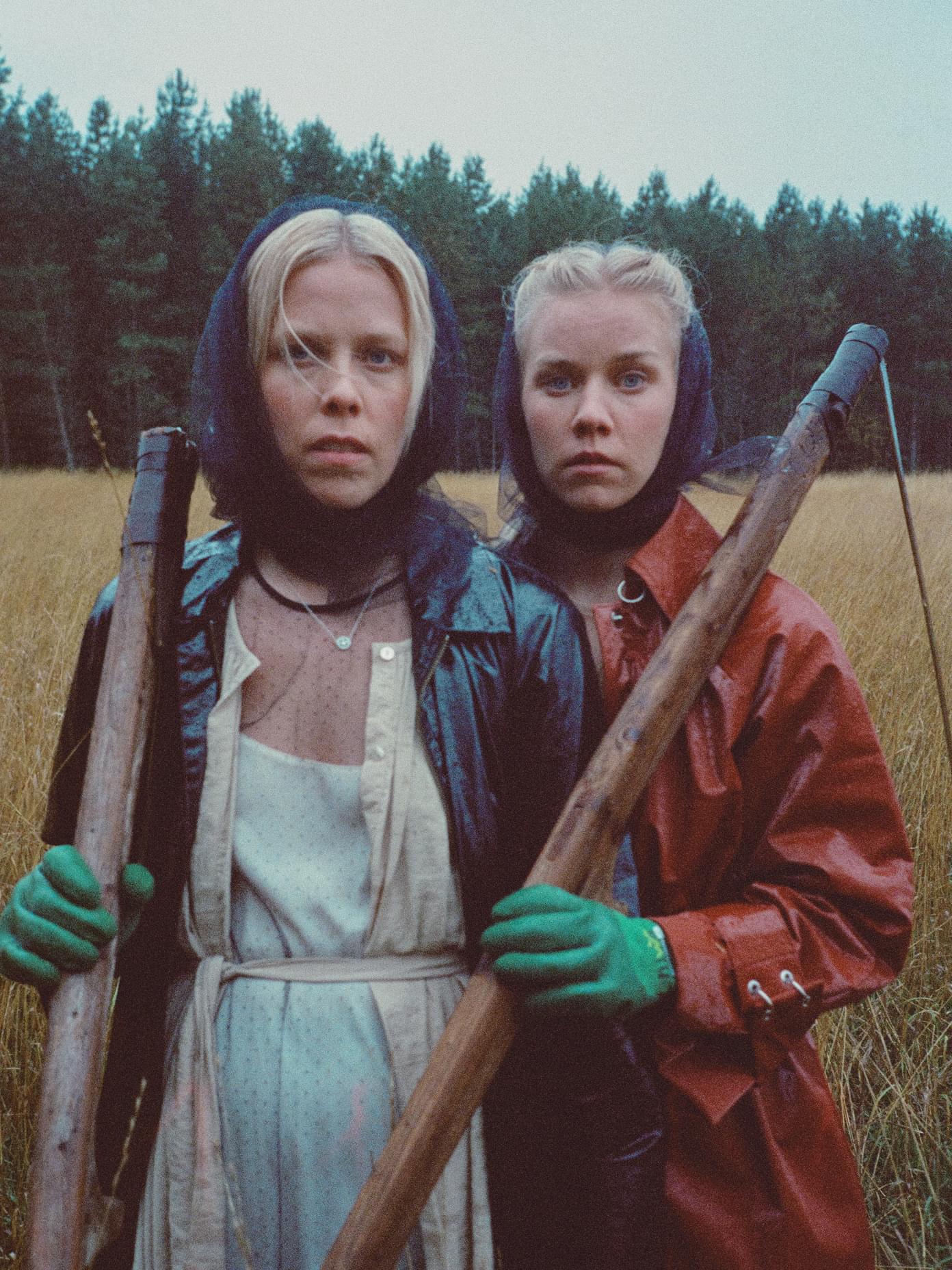 Two blonde women in rain gear holding wooden tools stand in a golden field for Mö, shot by Werklig.