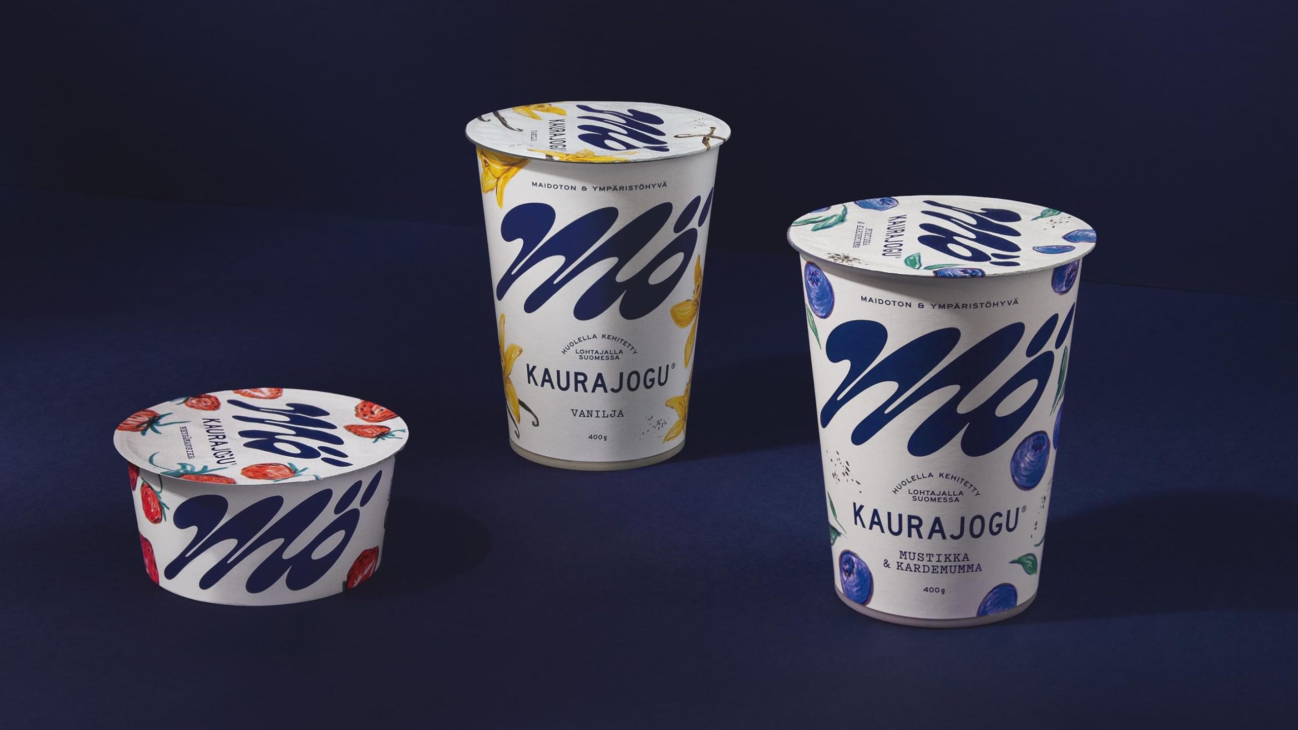 Three Mö Kaurajogu oat yogurt cups in vanilla, blueberry-cardamom, and strawberry flavors on a dark blue background.