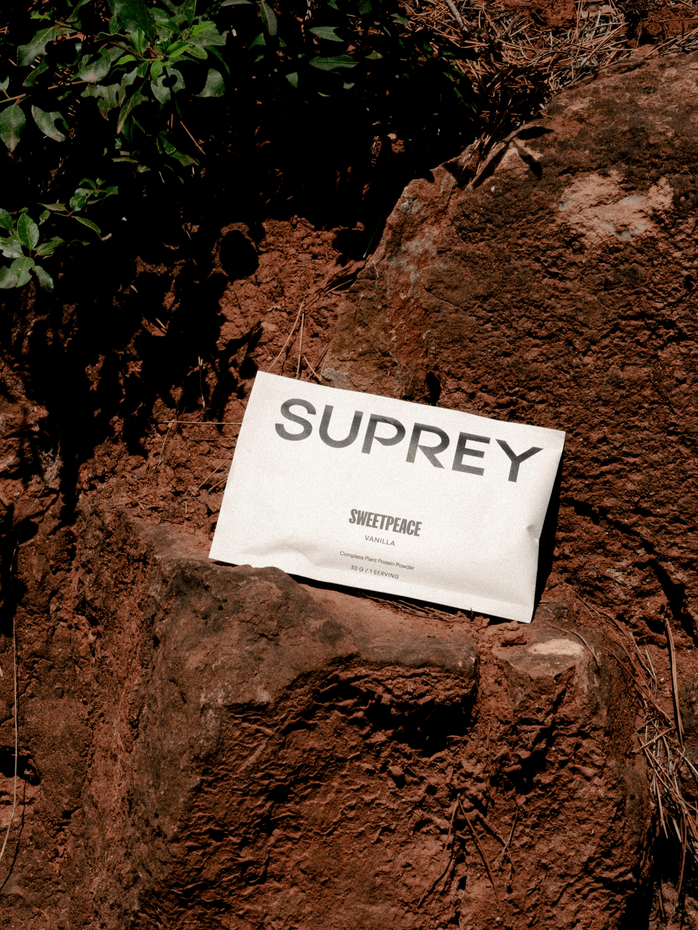 Suprey SweetPeace Vanilla plant protein powder sachet resting on red earthen rocks outdoors.