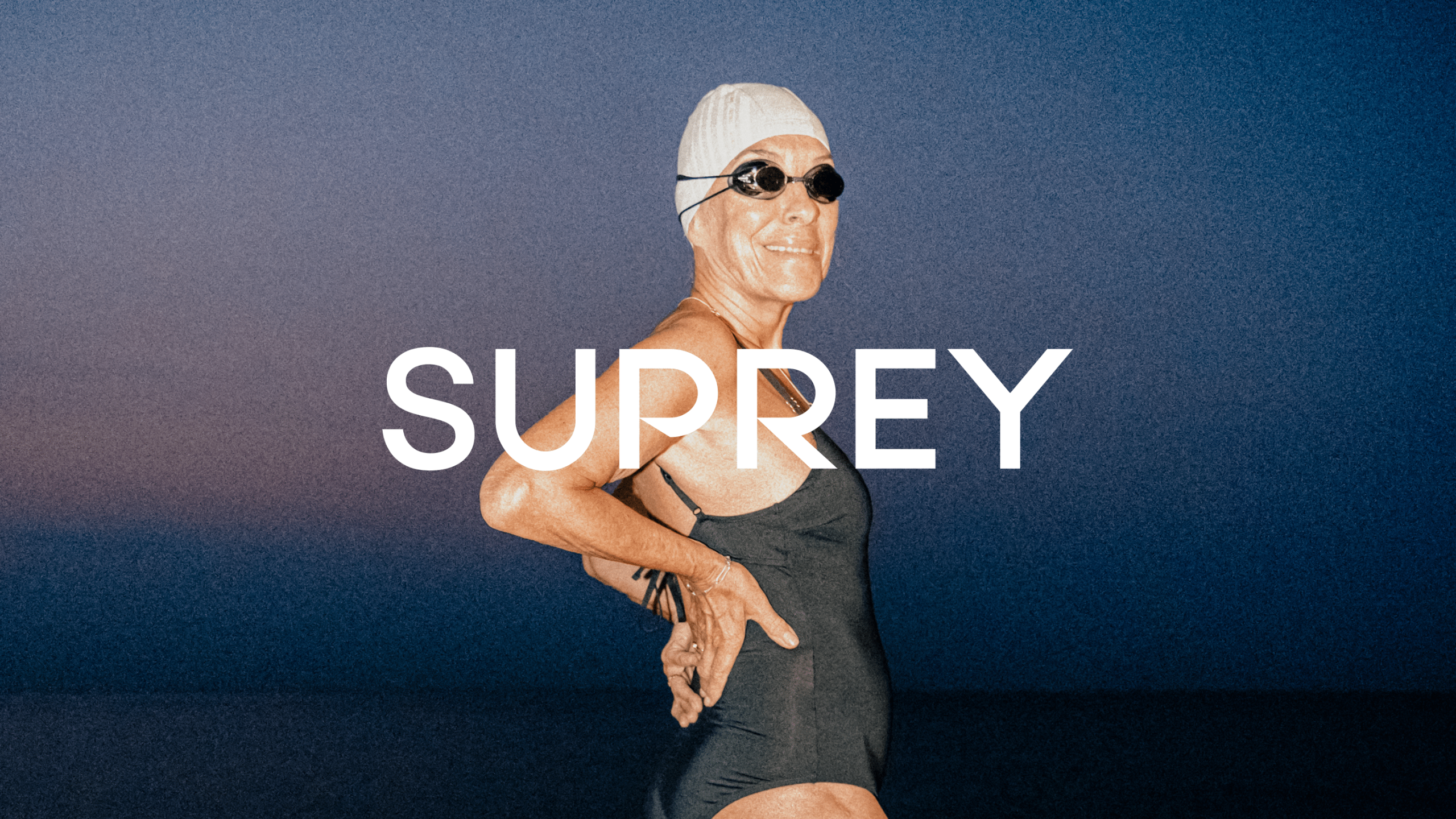 Older woman in black swimsuit, white cap, and goggles poses confidently against a dusk sky for Suprey's brand campaign.
