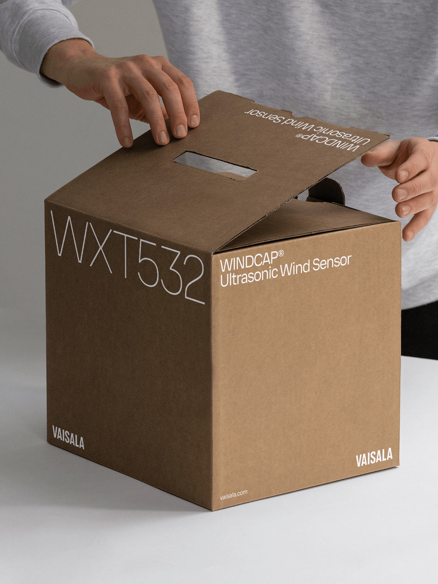 Hands opening a brown kraft cardboard box for Vaisala.