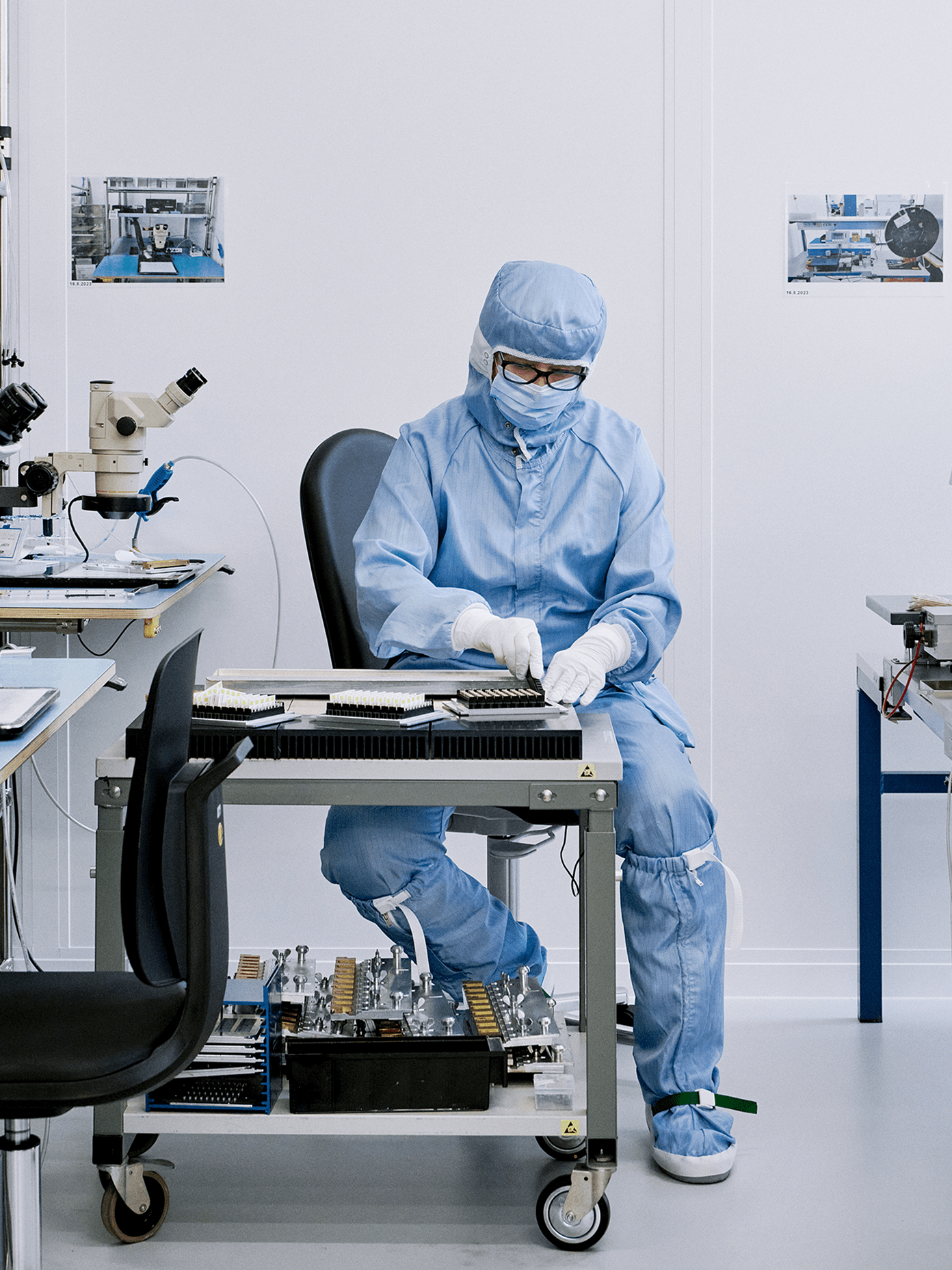Vaisala cleanroom technician in blue protective suit handling precision components at a mobile workstation.