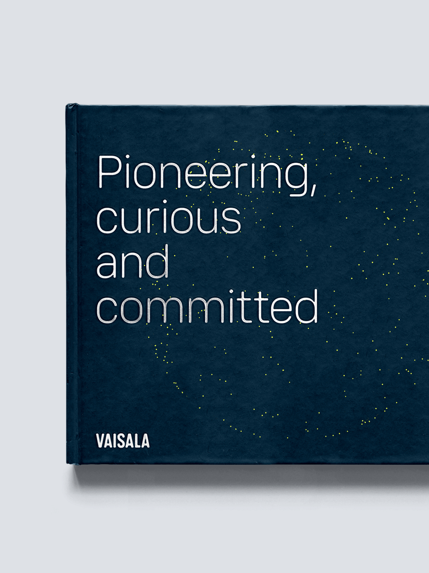 Vaisala hardcover book with dark navy cover, reading 'Pioneering, curious and committed' with yellow dot pattern.
