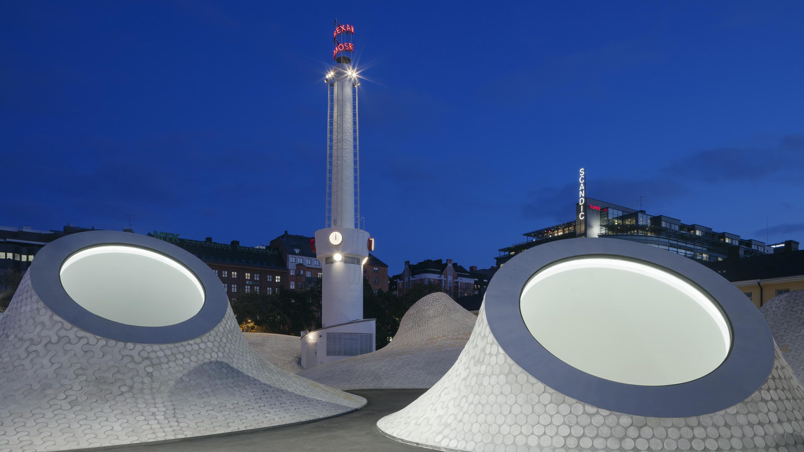 Amos Rex museum's dome-shaped rooftop mounds and the illuminated Lasipalatsi tower at night in central Helsinki.