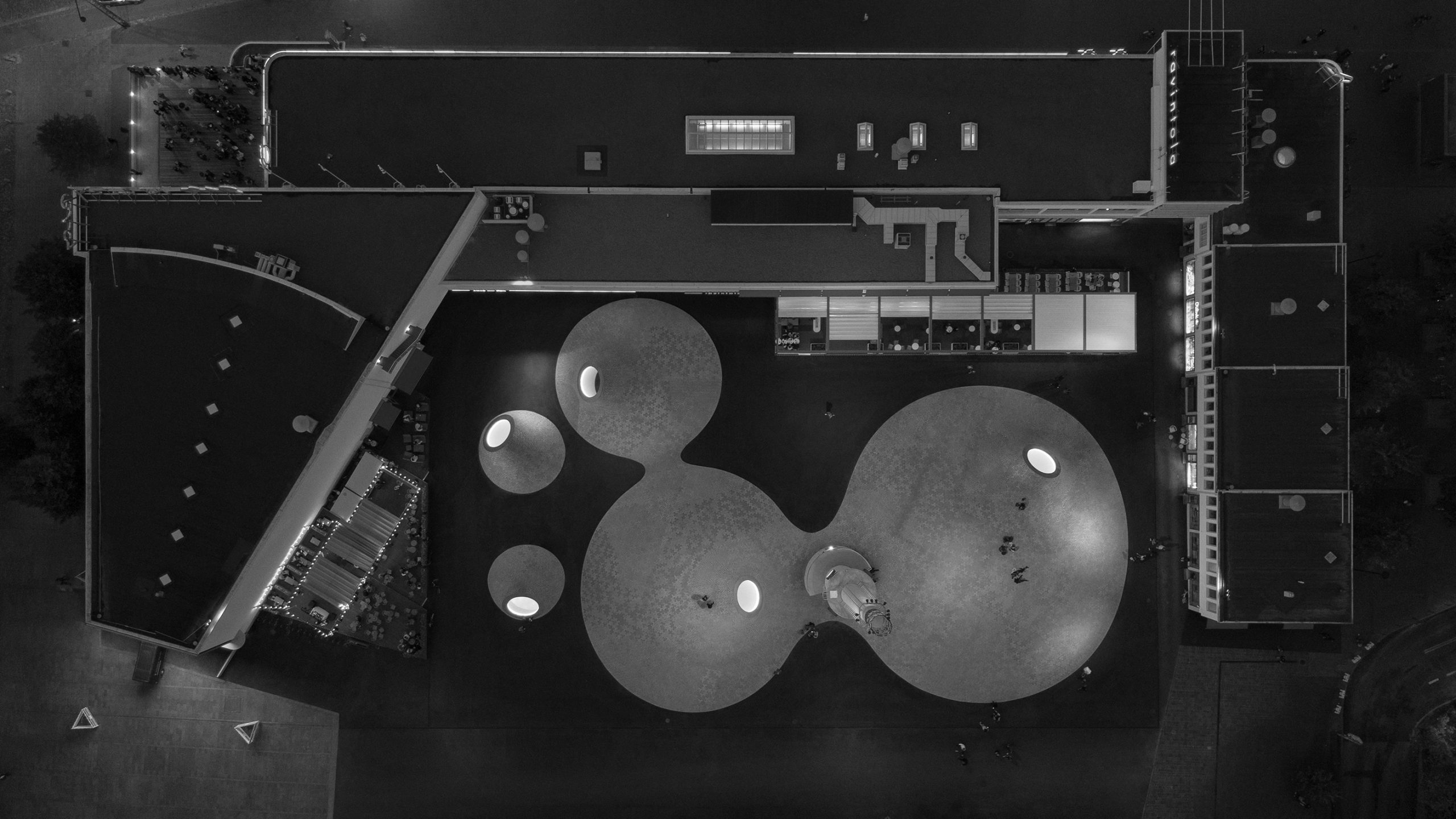 Aerial black-and-white night view of Amos Rex's plaza, showing illuminated dome skylights and the surrounding Lasipalatsi building.