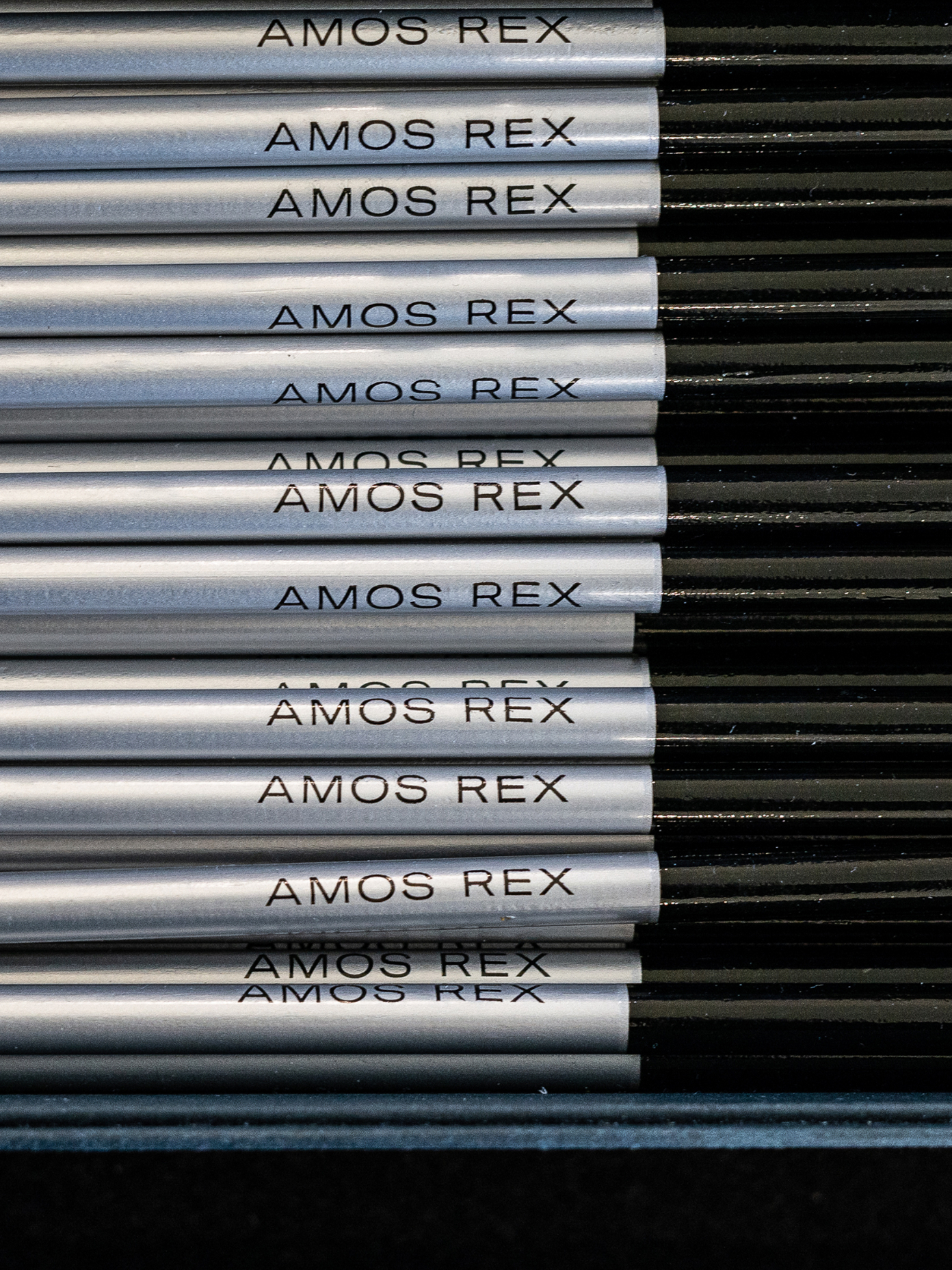 Rows of silver pencils printed with the Amos Rex wordmark in black type.
