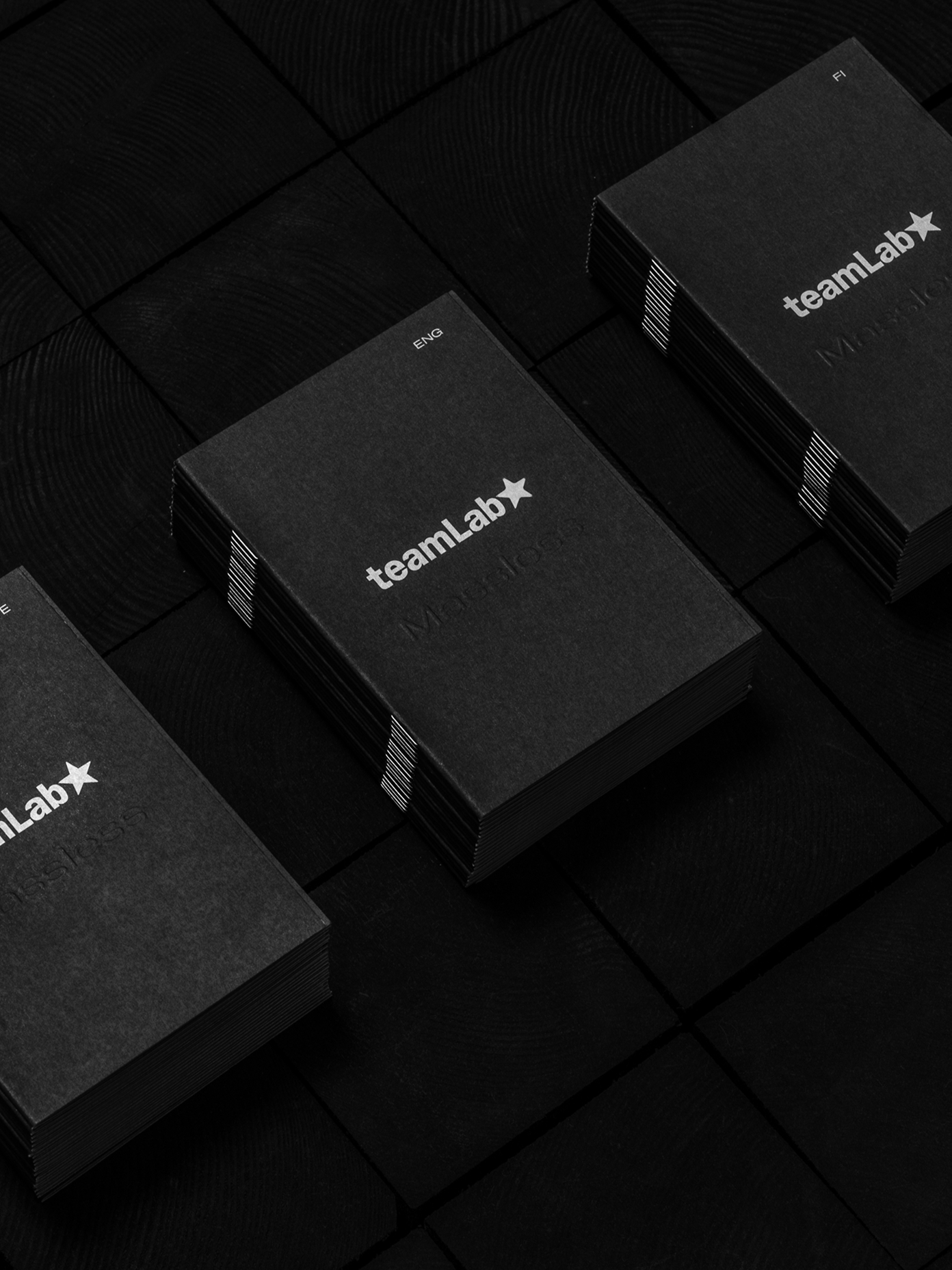 Stacked dark grey booklets embossed with the teamLab logo, marked for different language editions.