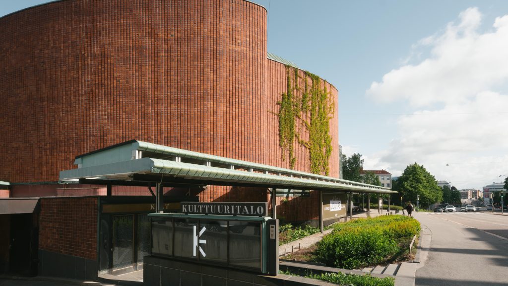 Kulttuuritalo's curved red brick façade with ivy climbing the walls and a canopy entrance bearing the building's name.