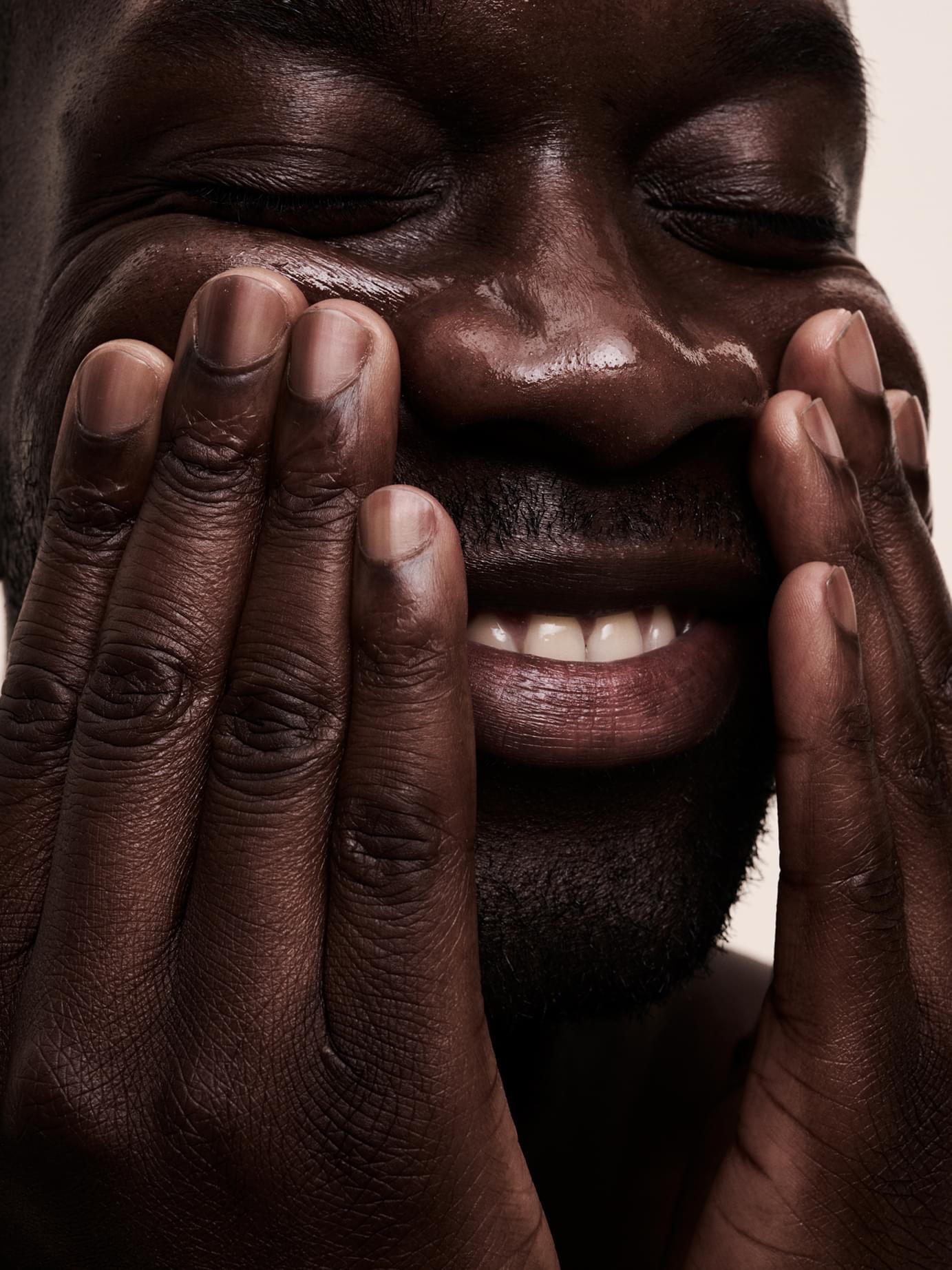 Close-up of a smiling person applying skincare with both hands, face glistening with product, for Blank& branding by Werklig.