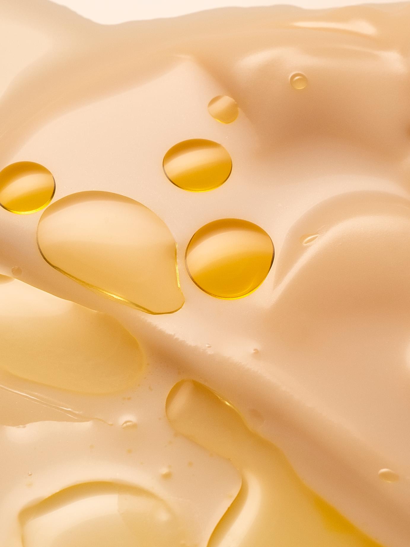 Close-up of golden oil droplets resting on a creamy beige lotion smear for Blank& branding by Werklig.
