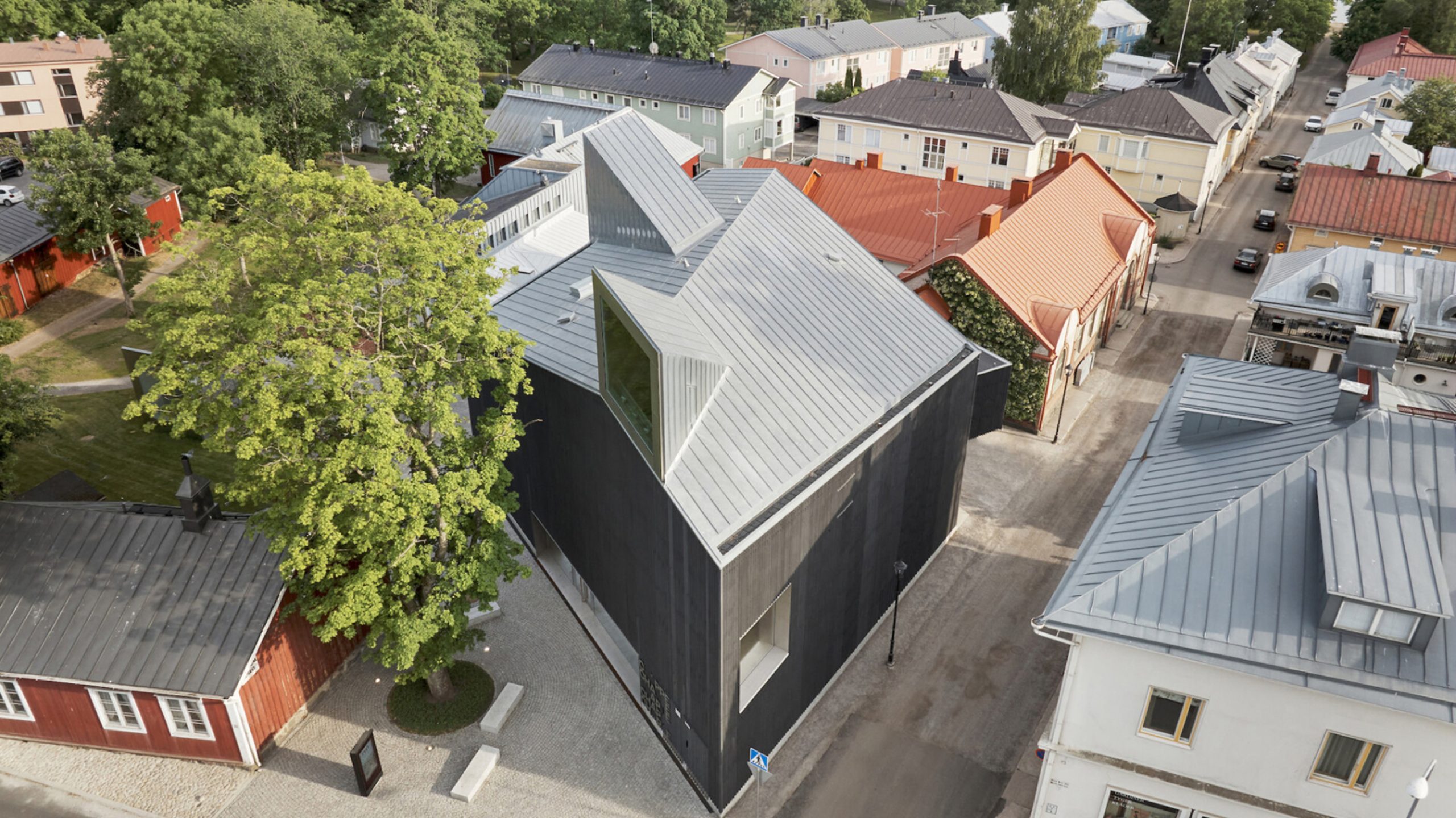 Aerial view of Chappe's dark timber building with angular zinc roof amid colorful Finnish townscape.