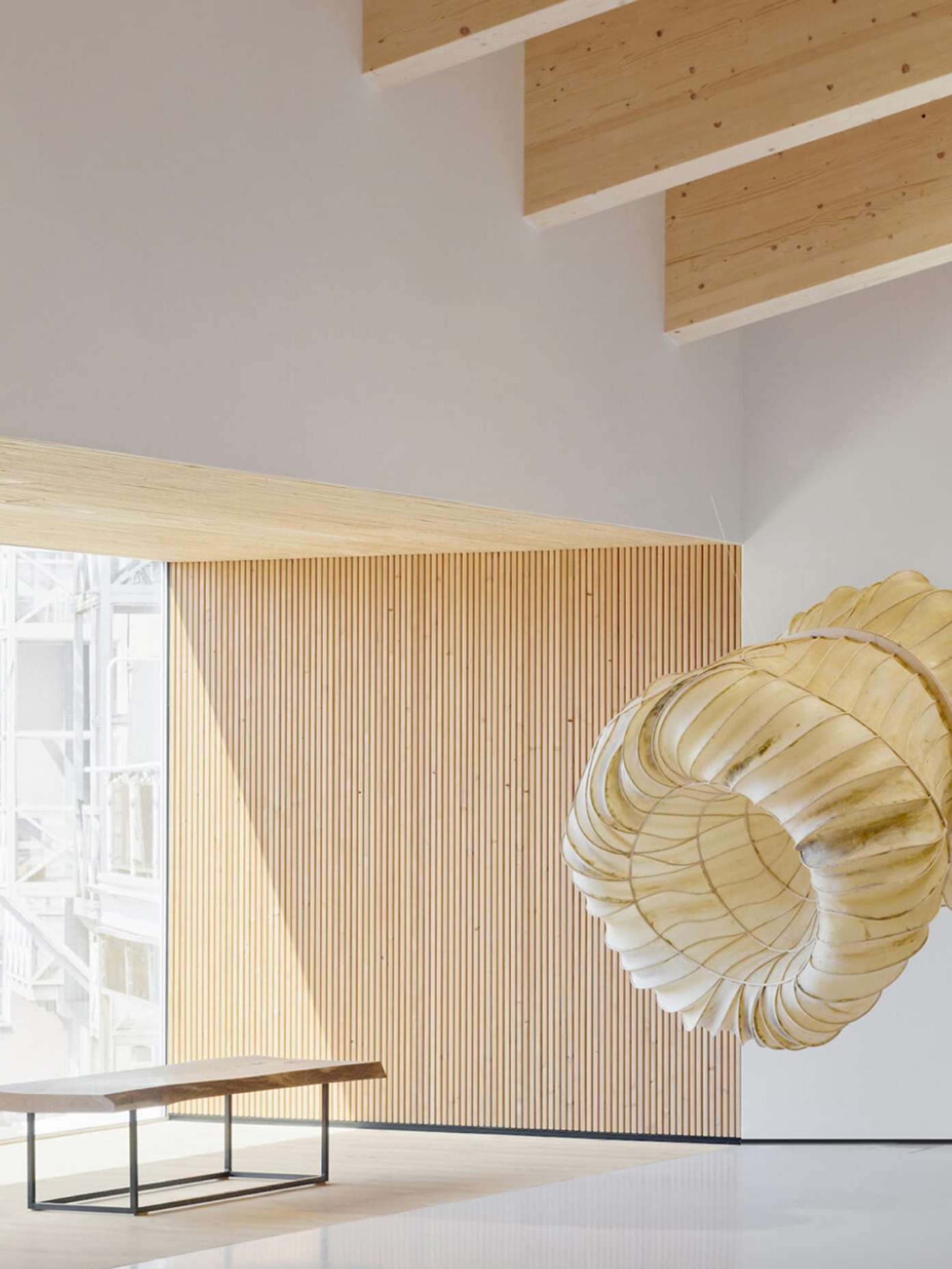 Chappe interior with vertical wood slat wall, exposed timber ceiling, a bench, and a large sculptural pendant light.