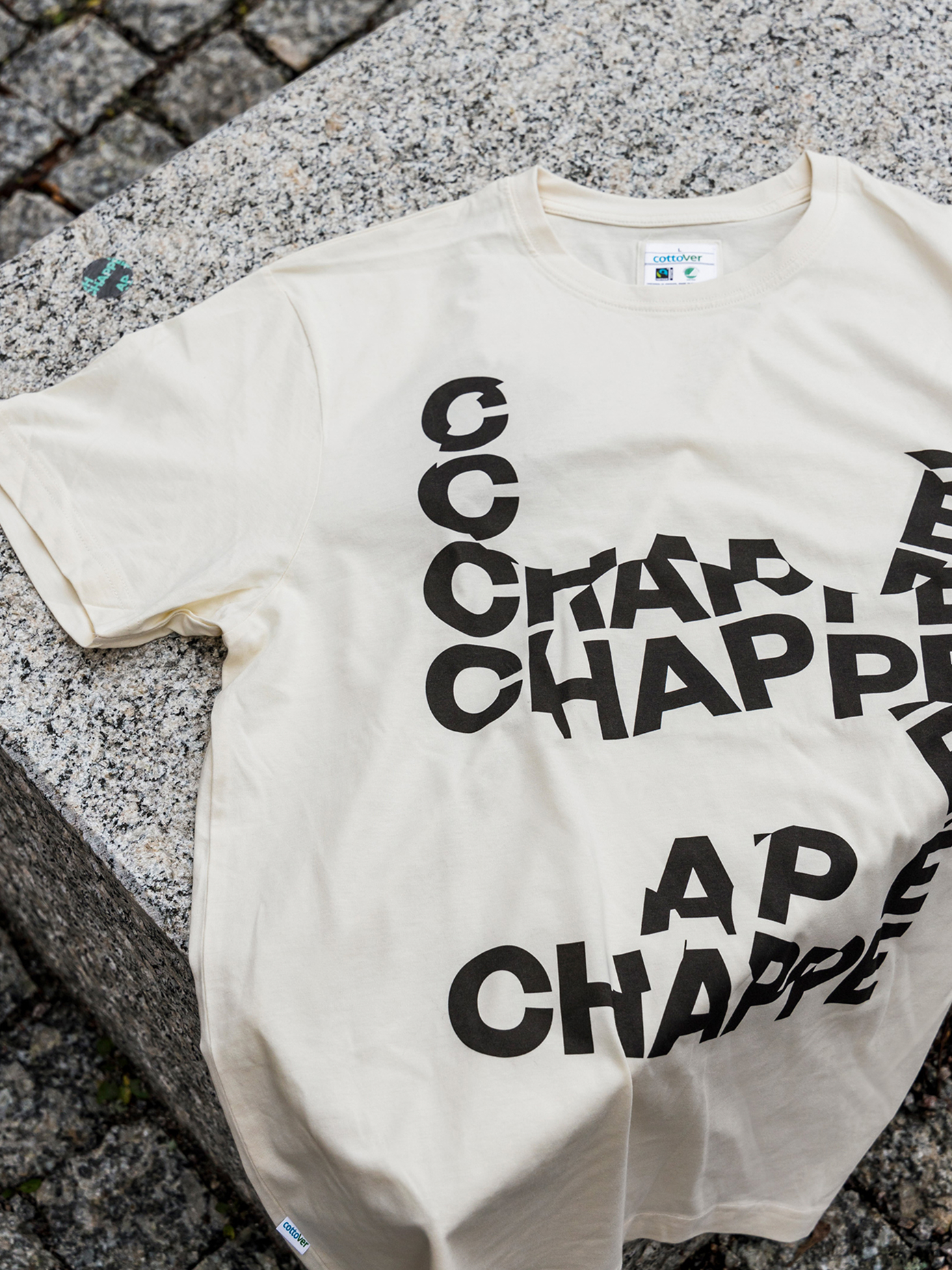 Cream Chappe branded t-shirt laid flat on granite steps, featuring bold black repeated typographic logo print by Werklig.