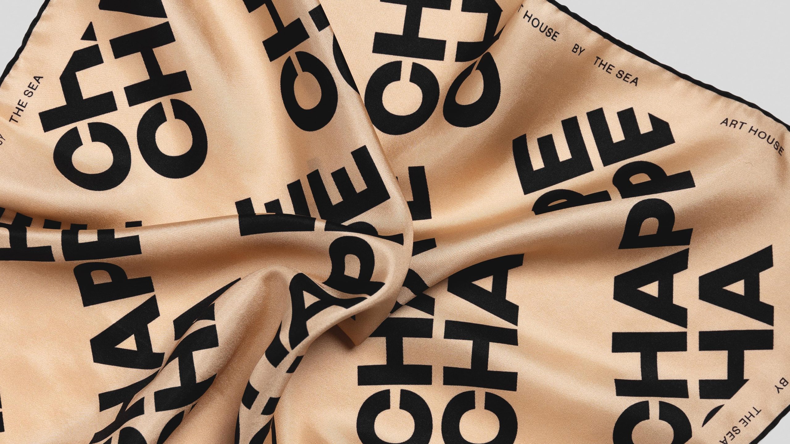 Chappe Art House by the Sea branded silk scarf in sand and black, featuring bold repeating typographic pattern.