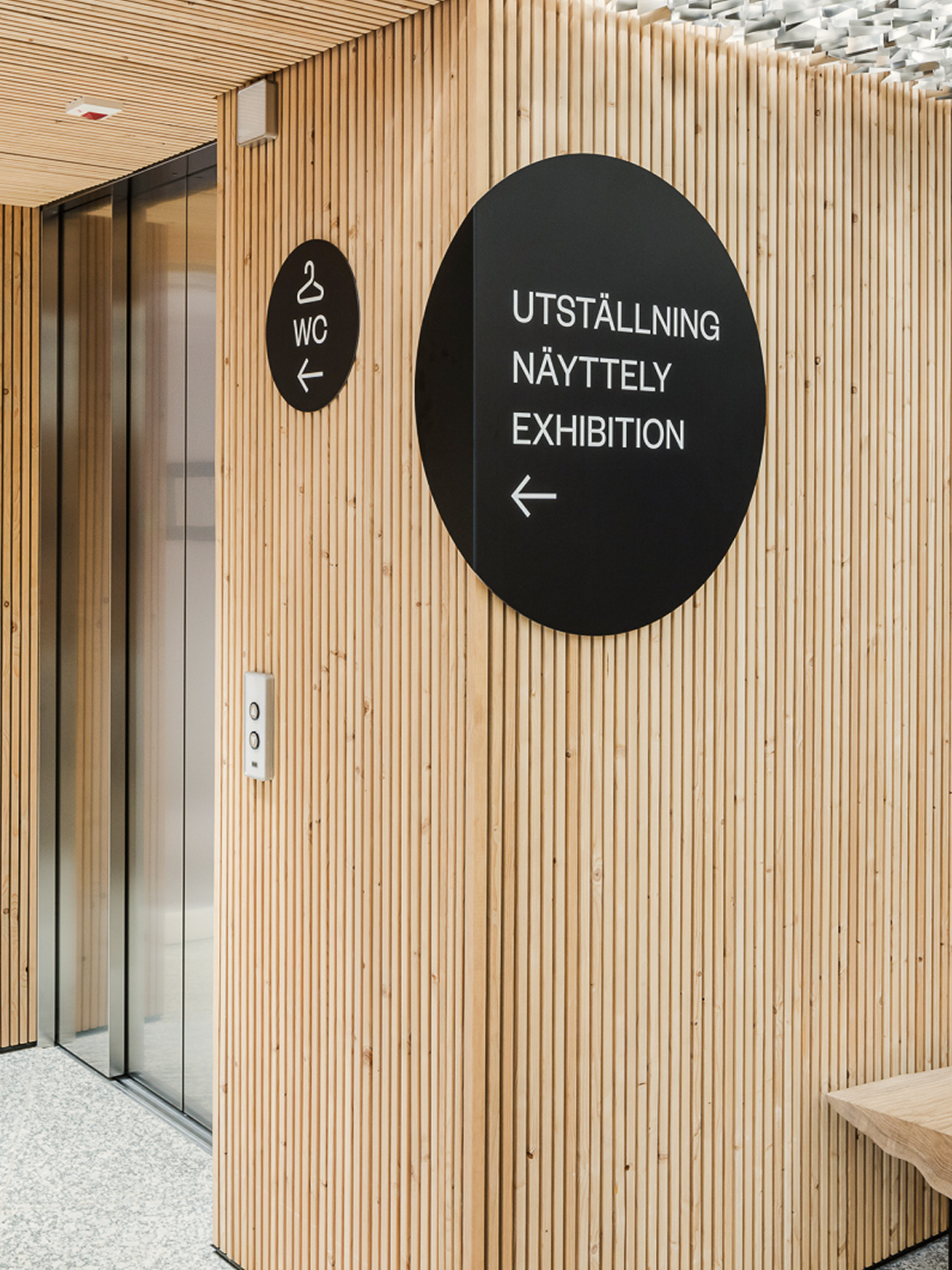 Chappe's signage on wood-slat wall with trilingual exhibition and WC signs in black circles.