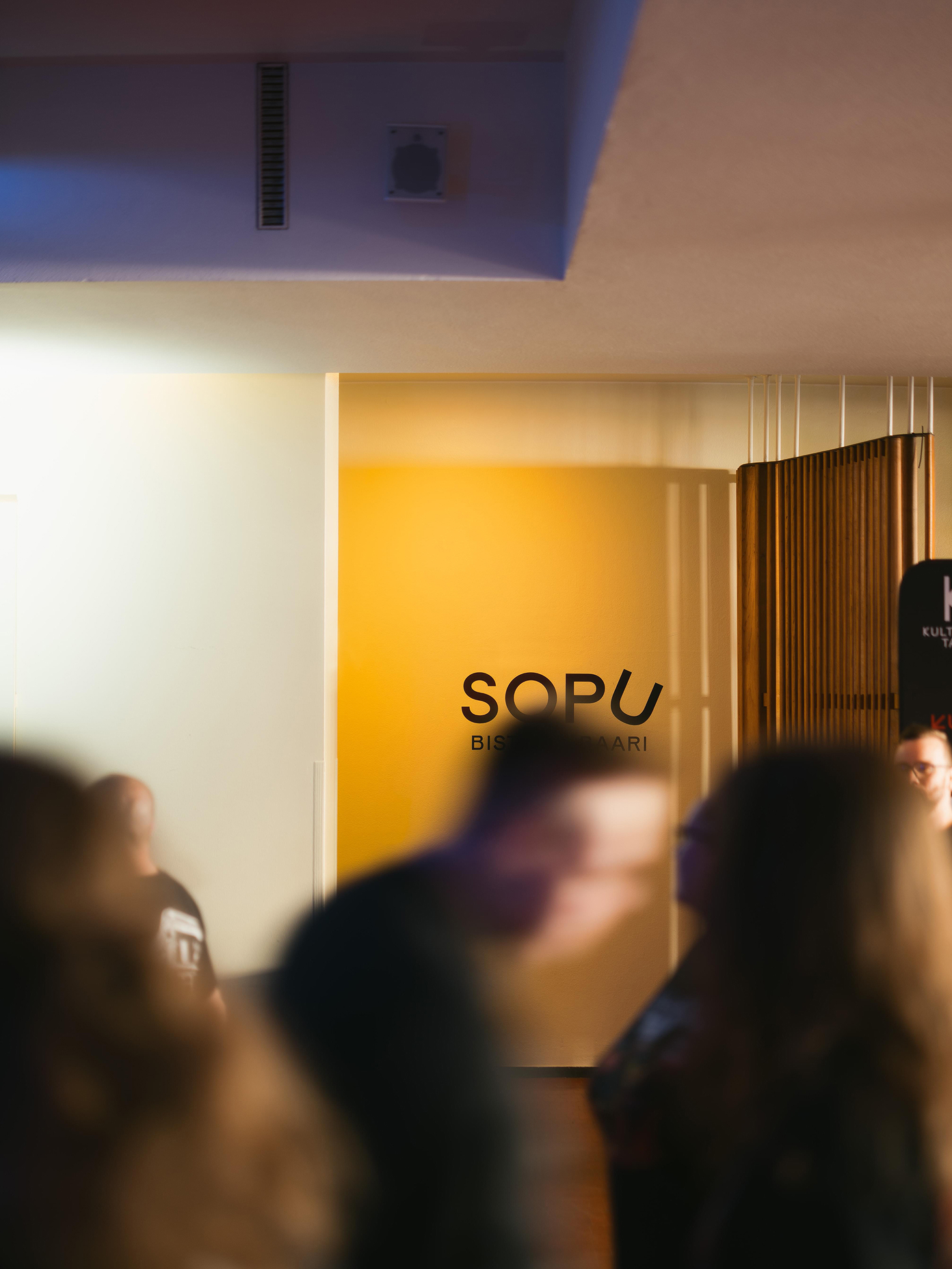 Sopu Bistrobaari signage on a yellow wall inside Kulttuuritalo, with a crowd of visitors in the foreground.