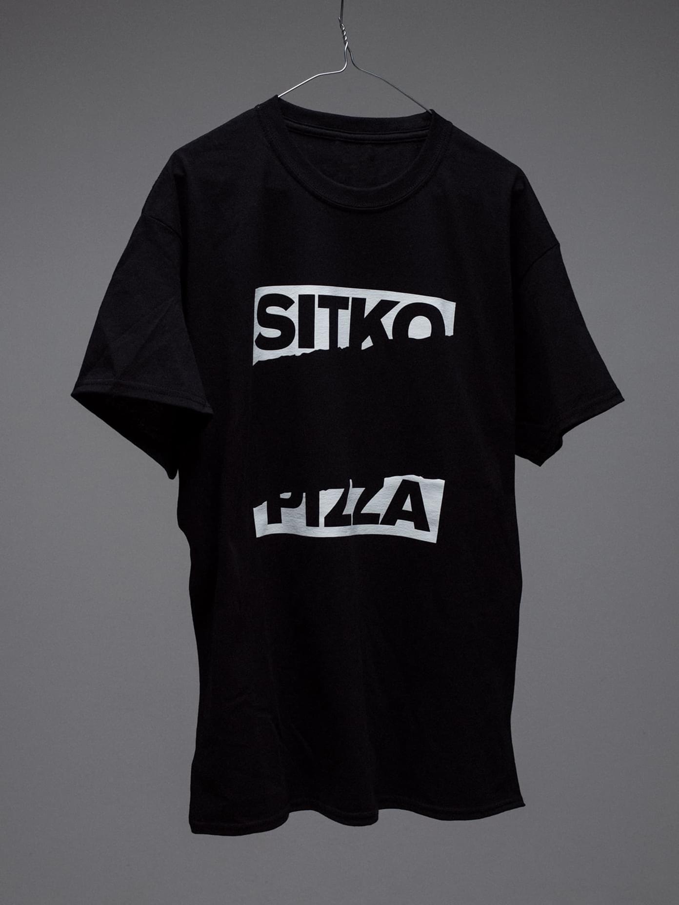 Black Sitko Pizza branded t-shirt with bold white rectangular logo graphics hung on a wire hanger against grey background.