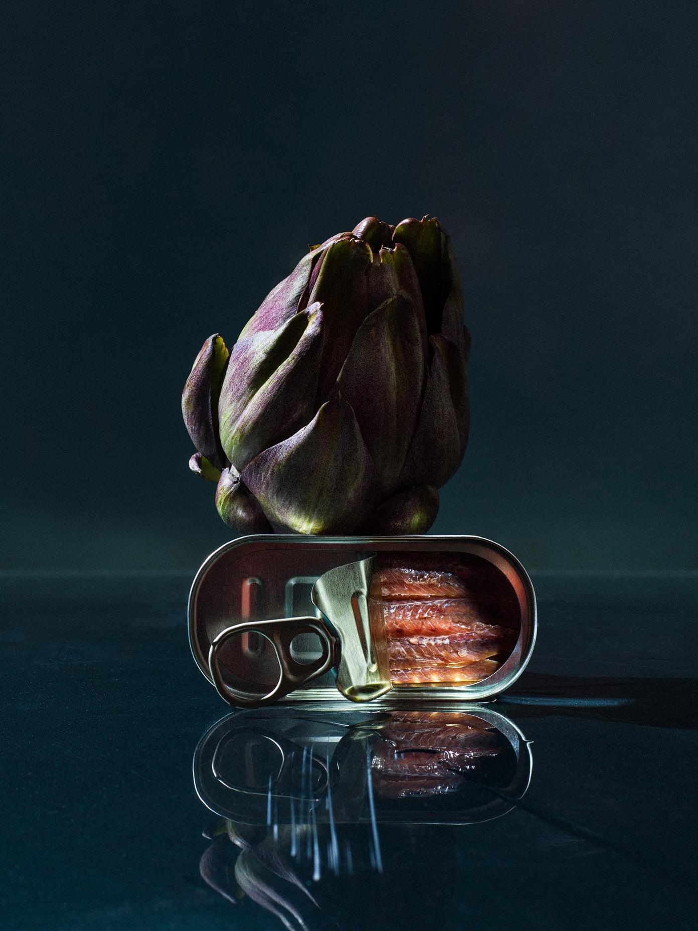 Artichoke balanced on an open tin of anchovies, reflected on a dark surface, from Werklig's Sitko Pizza branding project.