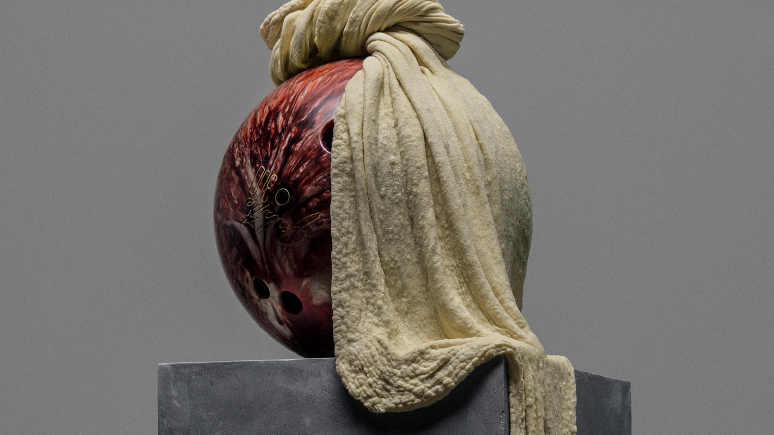 A dark red bowling ball draped with a cream cloth on a stone pedestal, part of Sitko Pizza's brand identity by Werklig.