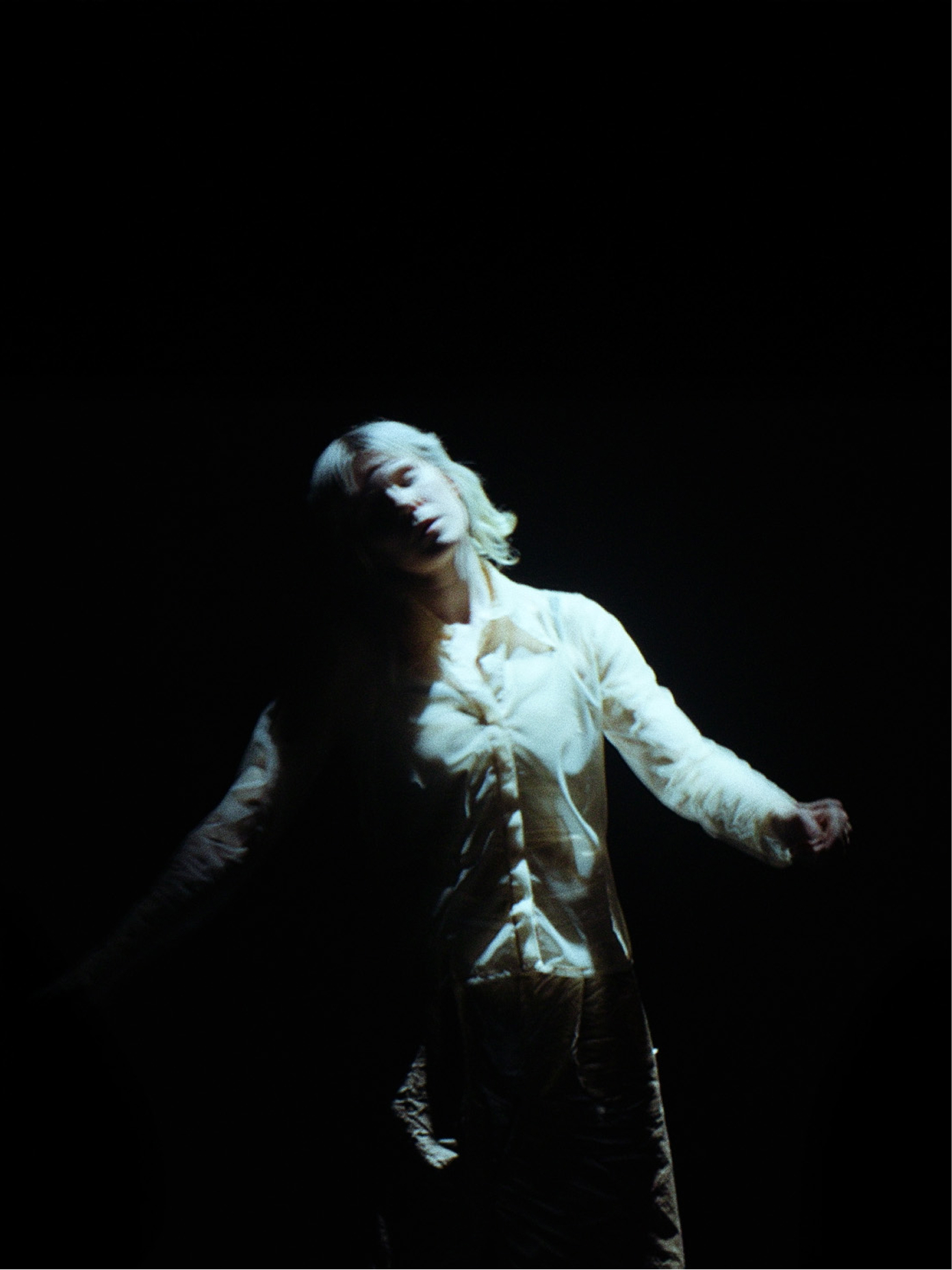 Tero Saarinen Company dancer in white ruffled shirt, head tilted back, arms outstretched, lit dramatically against black.