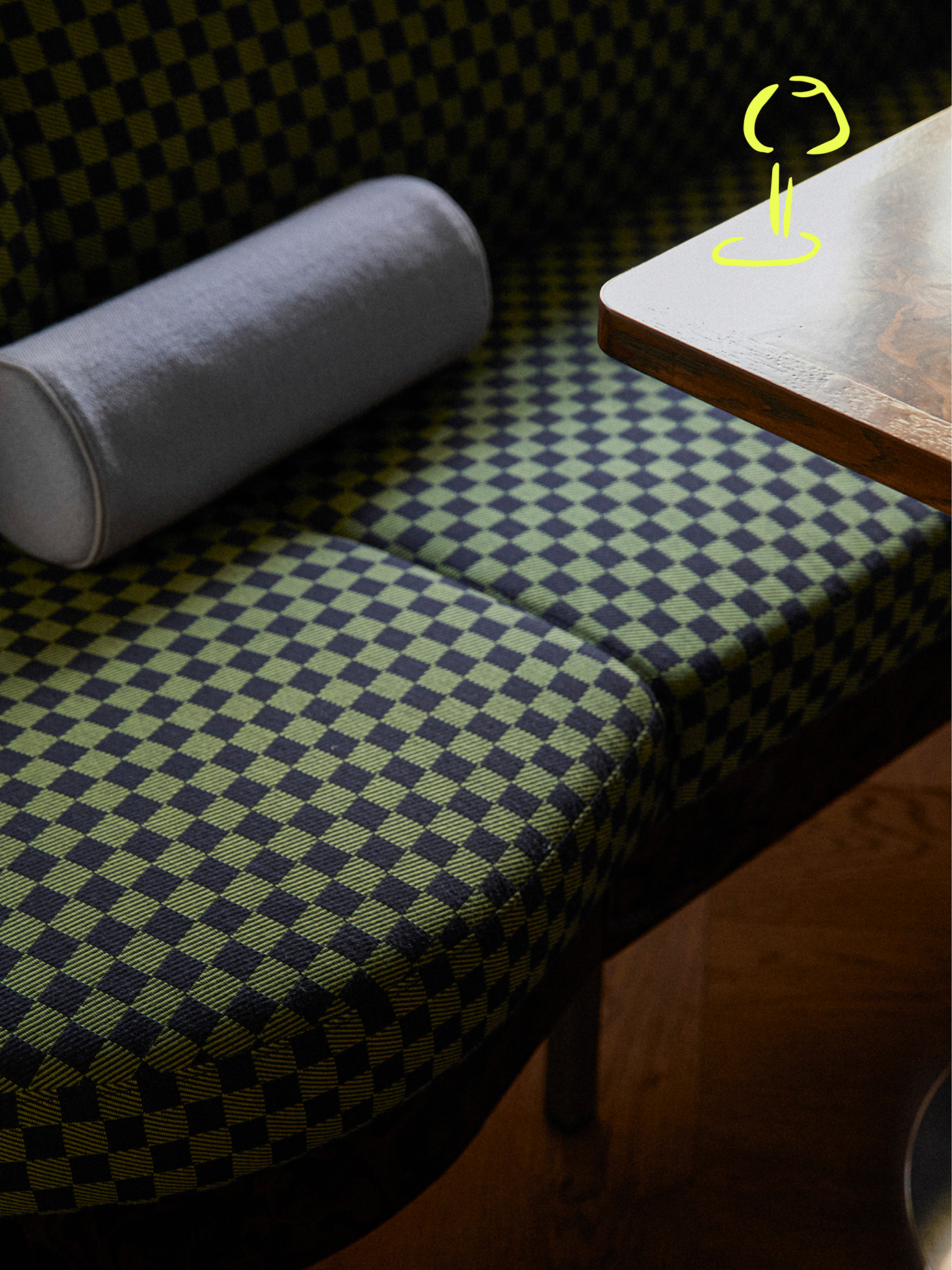 Green and navy checkerboard booth seating with a grey bolster pillow beside a dark wood table, marked with Teller's illustrated logo.