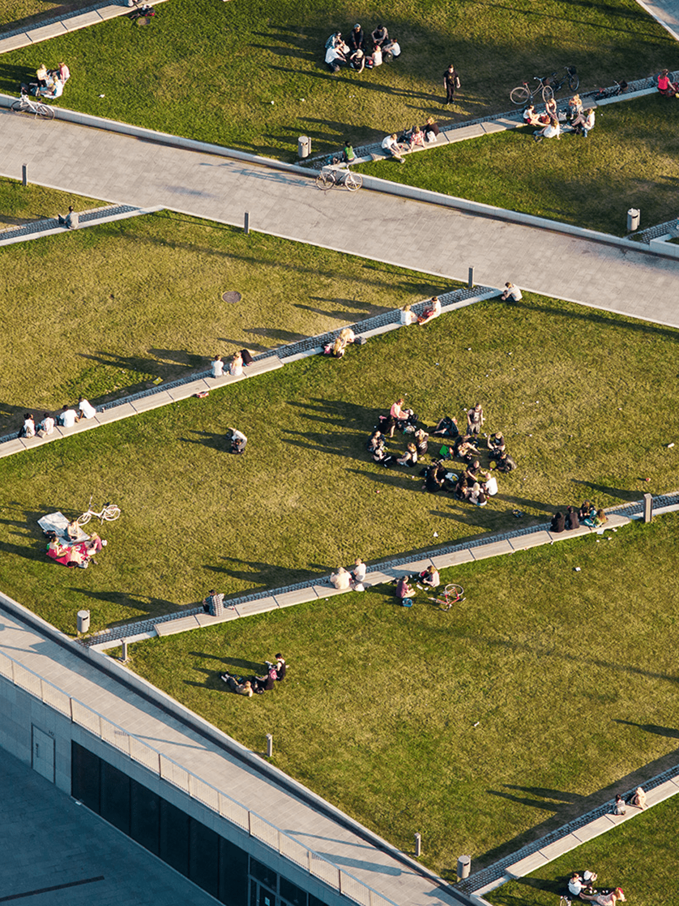Aerial view of people relaxing on grassy terraced rooftop with winding pathways on a sunny day in Helsinki.