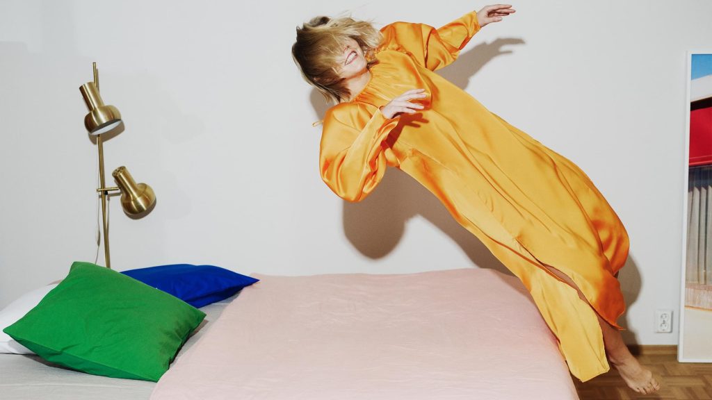 Person in orange satin dress jumping on a bed with colorful pillows, captured mid-air for Villa & Peite branding by Werklig.