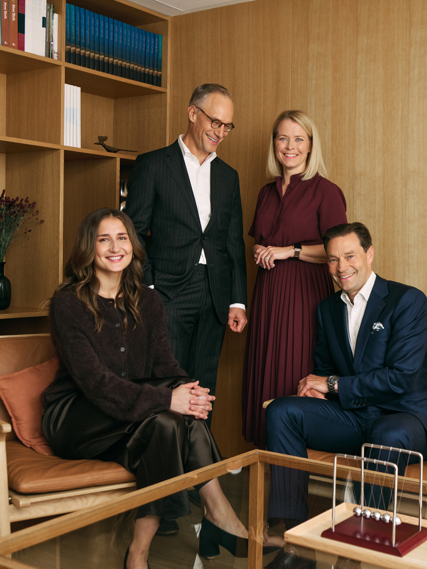 Four Avance team members posing in a warmly lit wood-panelled office with bookshelves and a Newton's cradle.