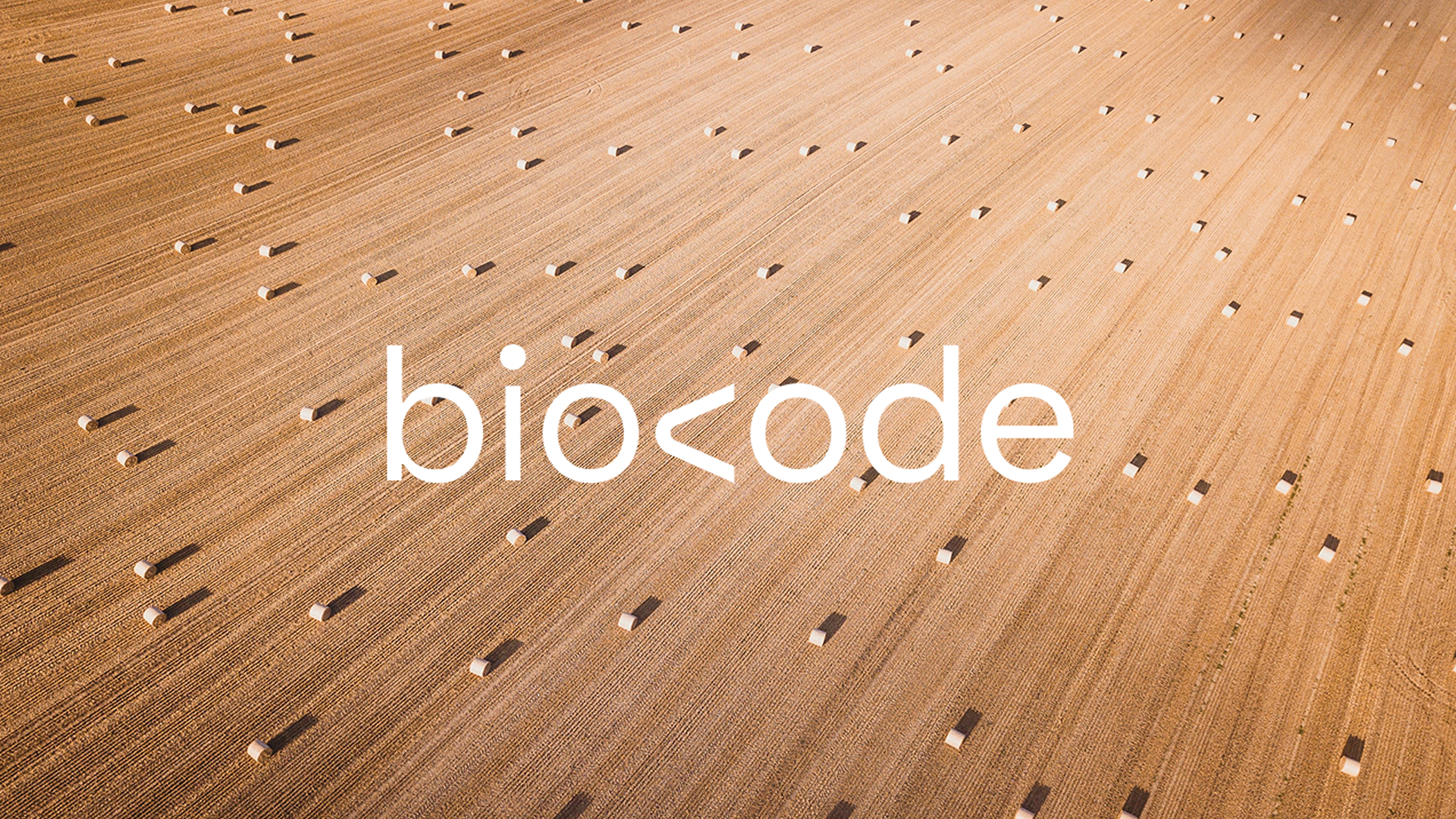 Biocode logo overlaid on an aerial view of a harvested field with scattered hay bales in warm golden tones.