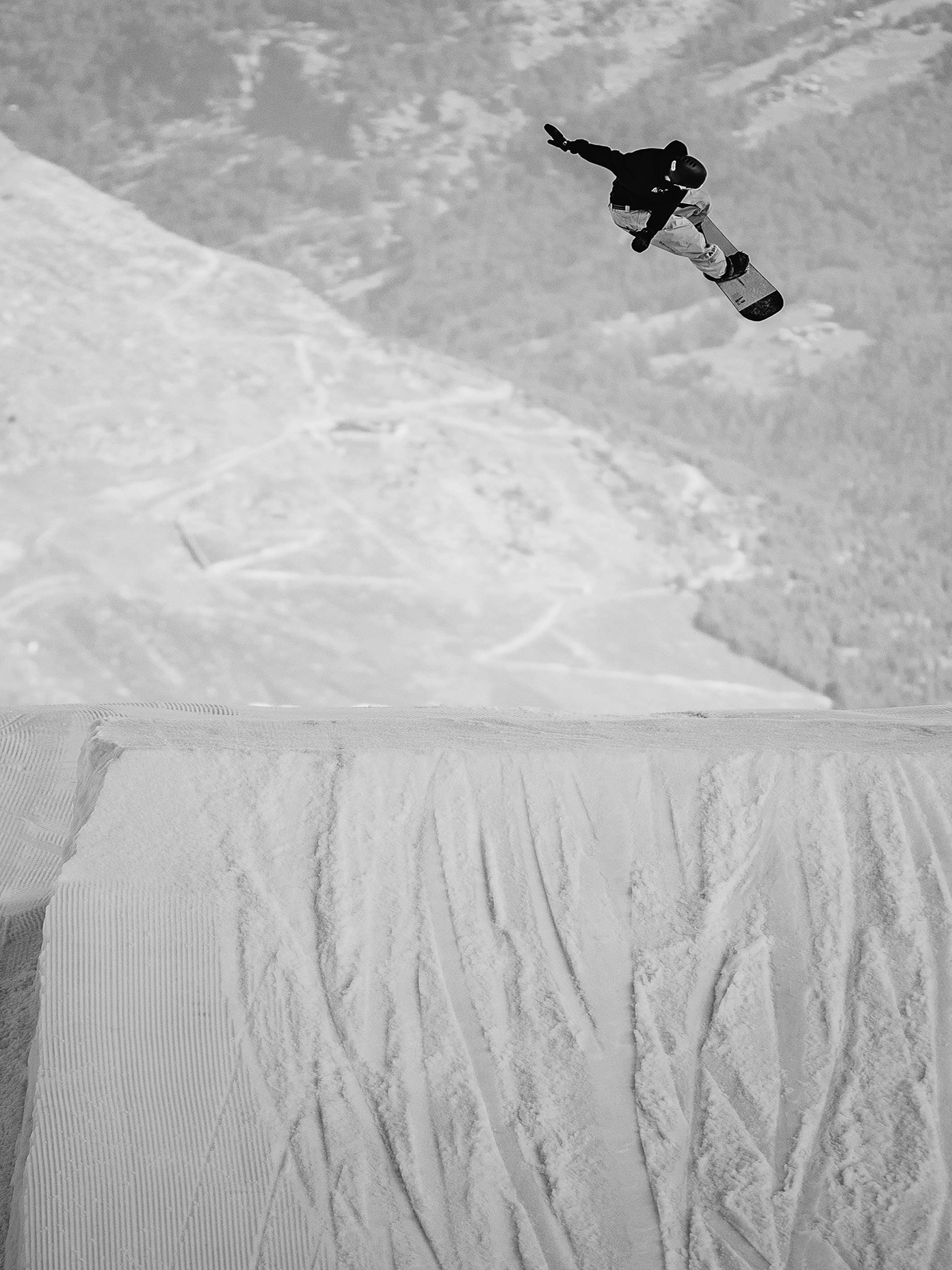 Snowboarder mid-air above a massive snow jump.