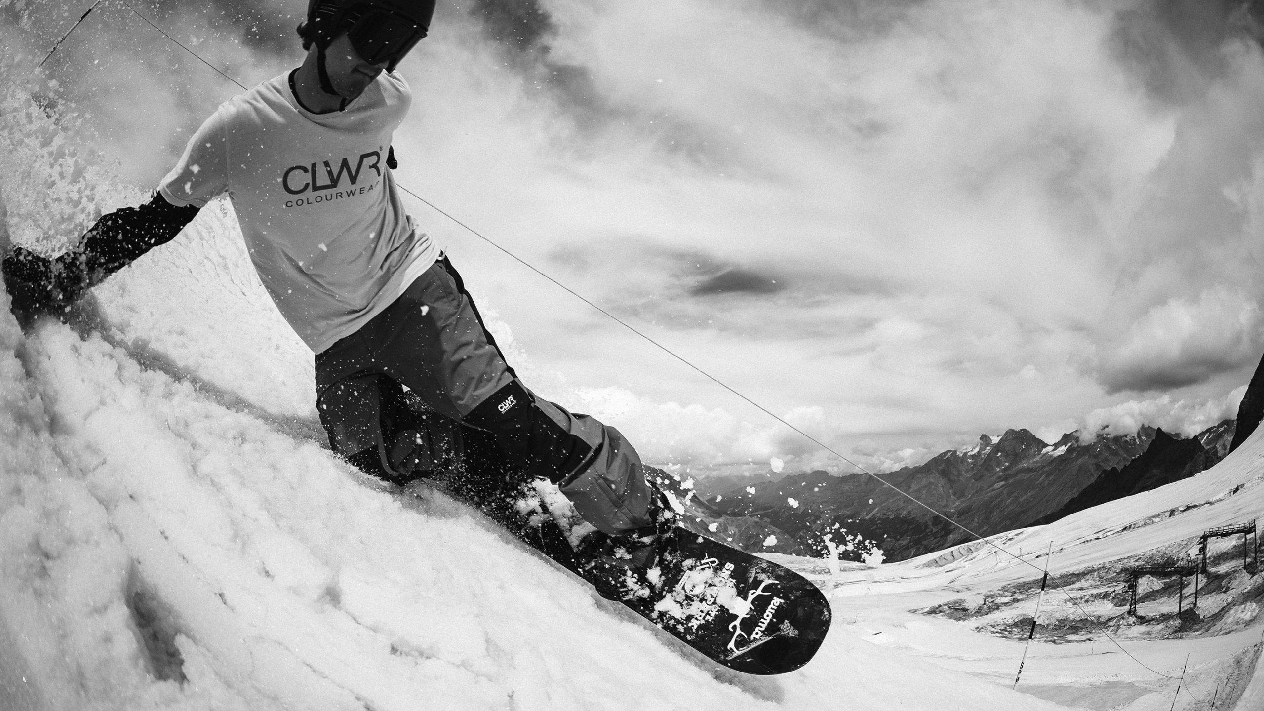 Snowboarder carving through snow with mountain peaks in background, black and white.
