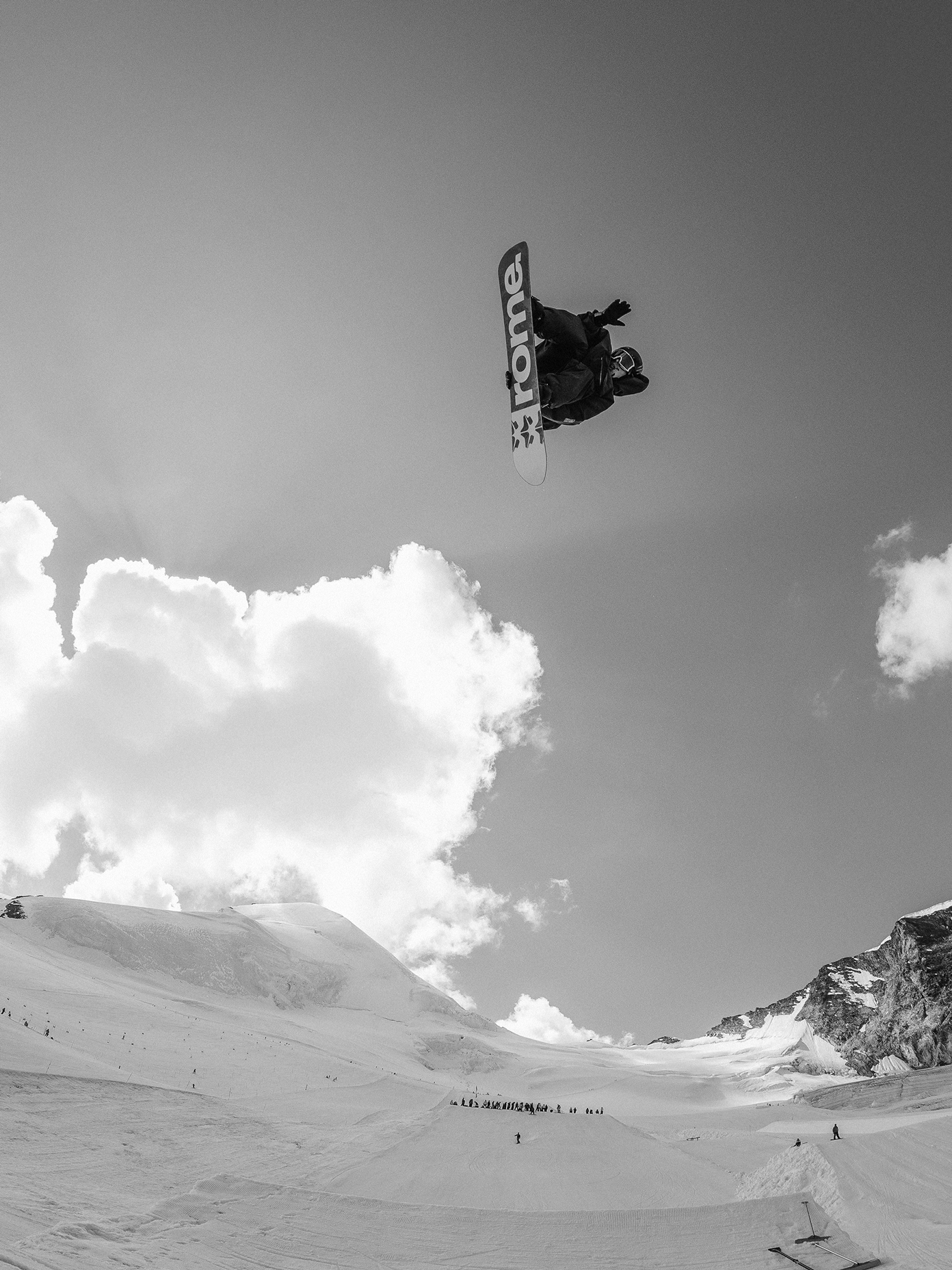 Snowboarder mid-air grab above a snow park, shot from below against a dramatic cloudy sky.