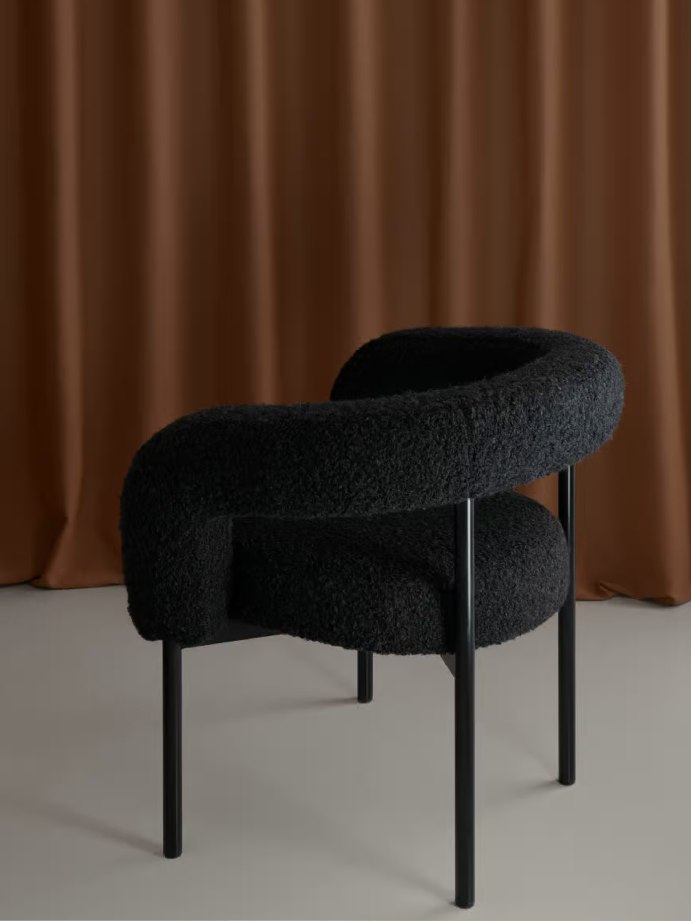 Boa chair in black bouclé fabric with tubular steel legs, photographed against warm terracotta draping.