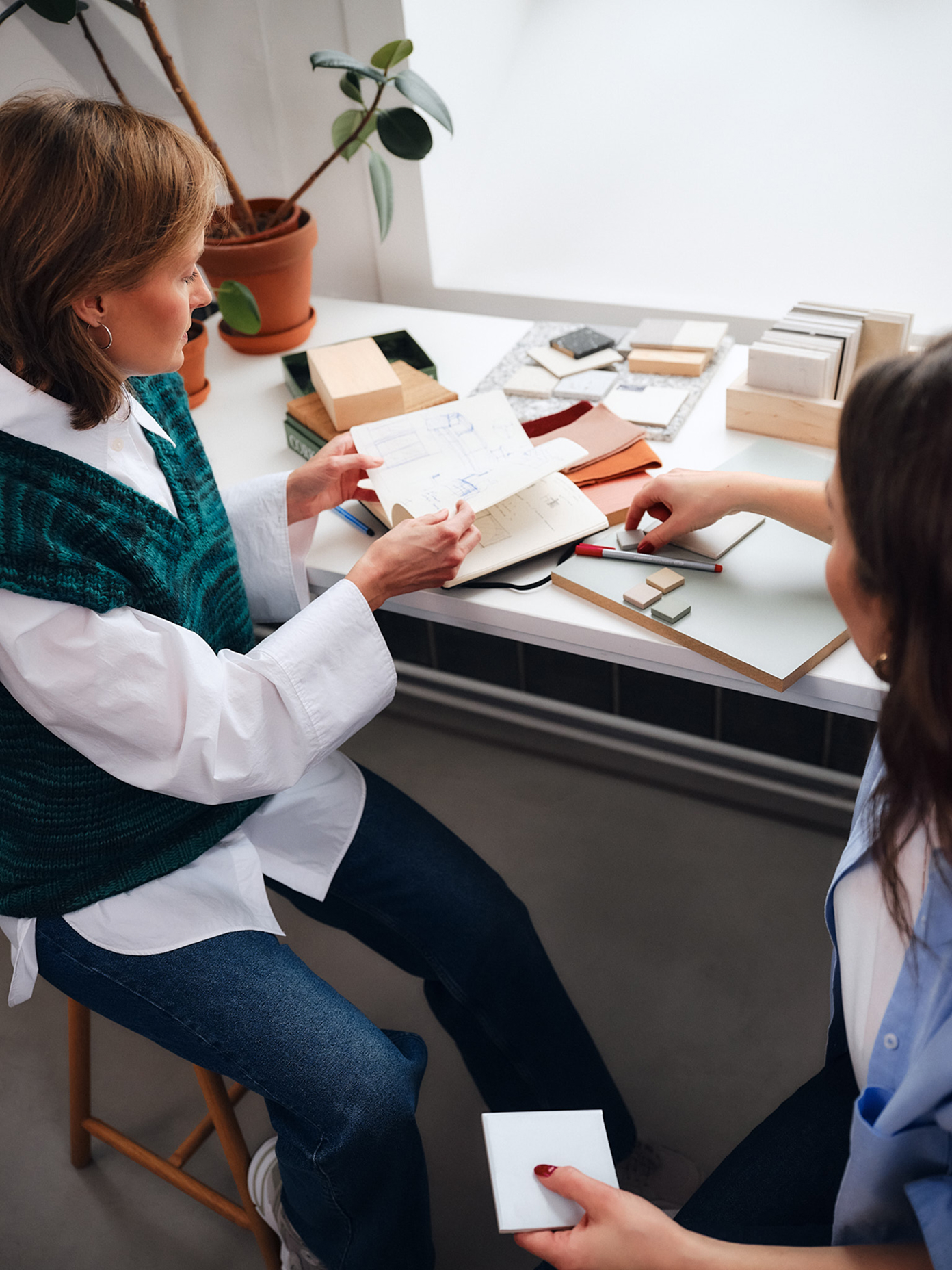 Two designers at Fyra review sketches and material samples on a studio desk, surrounded by swatches and stone tiles.