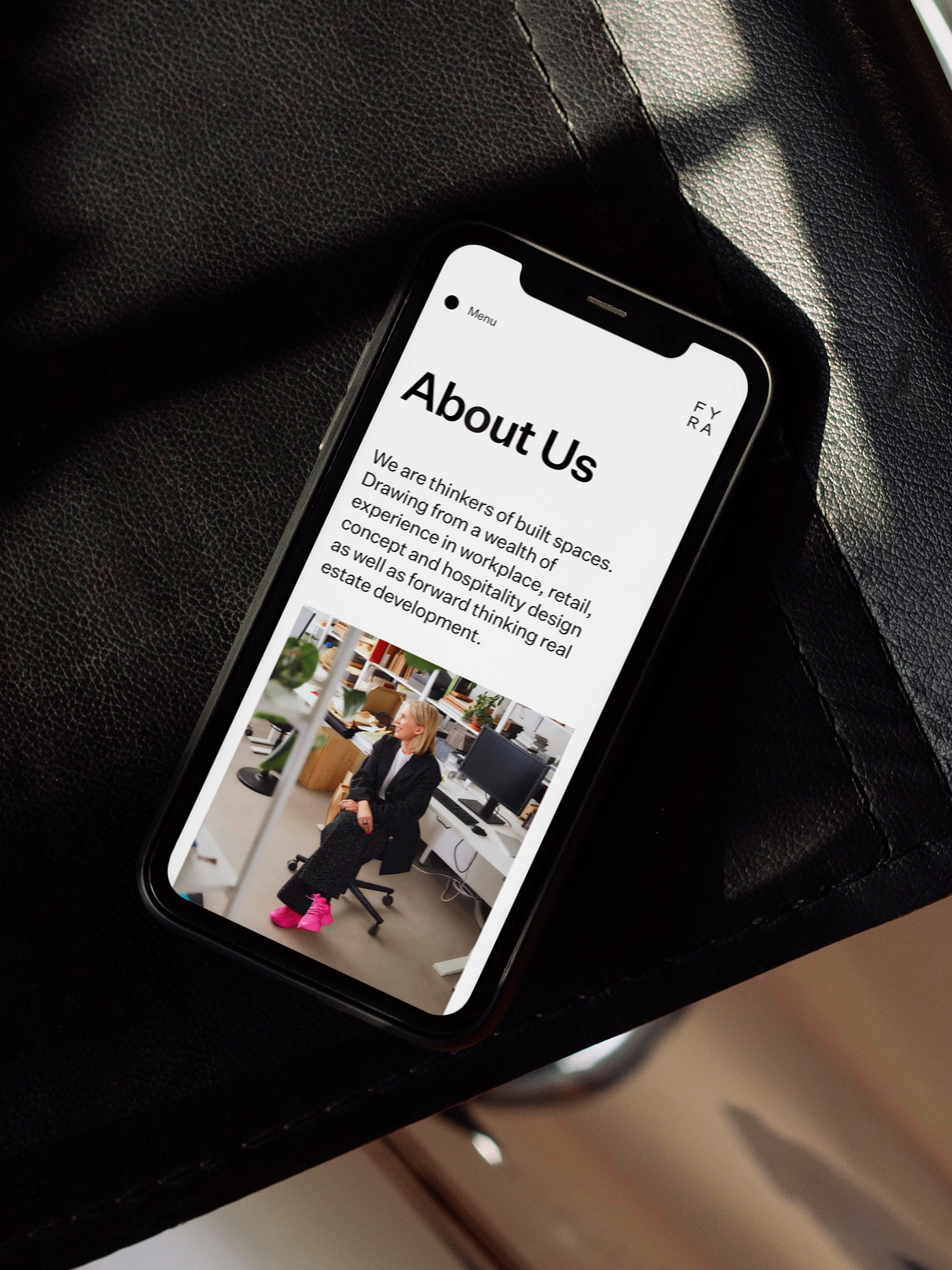 Fyra website 'About Us' page displayed on a black iPhone, resting on a dark leather surface.