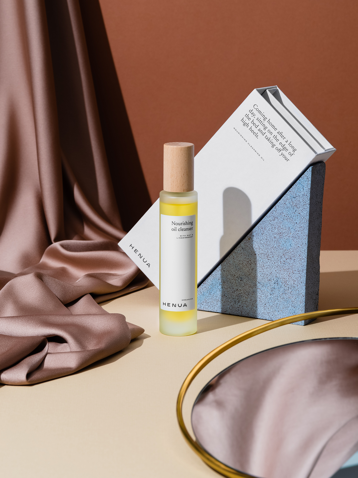 Henua Organics Nourishing Oil Cleanser bottle with wooden cap styled alongside branded packaging and draped fabric.