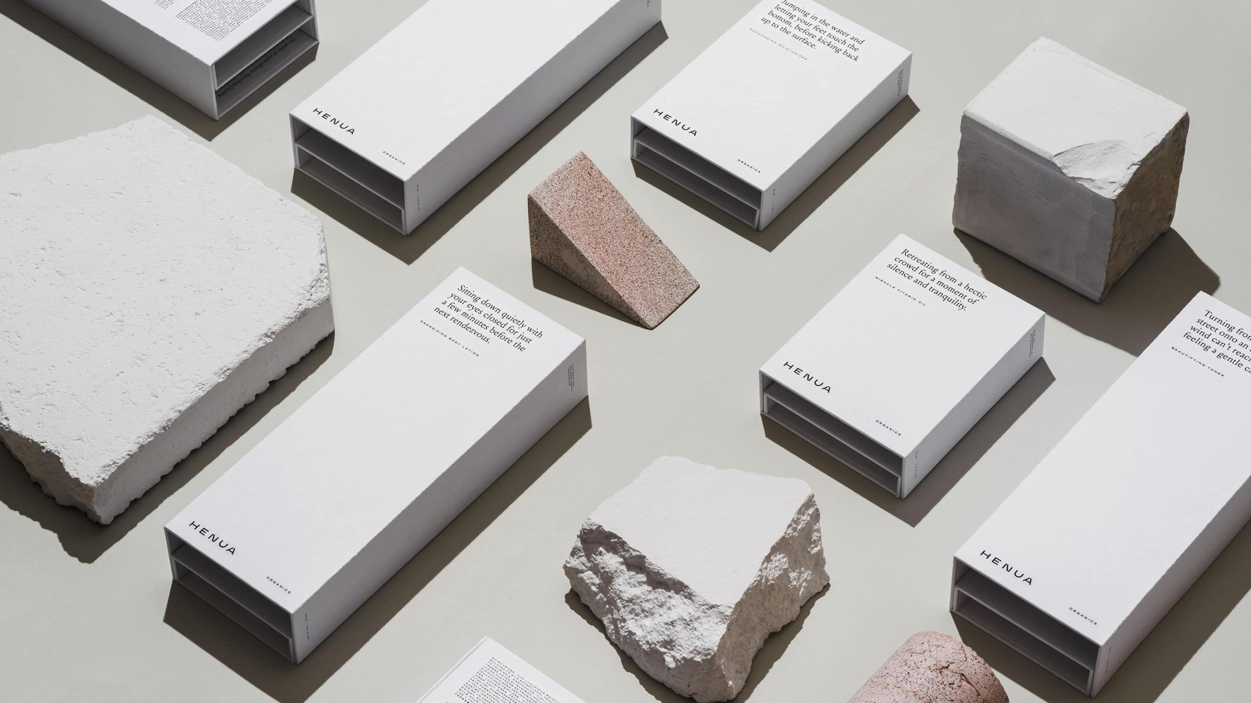 Henua Organics white product boxes arranged with rough stone and cork fragments on a pale green surface.