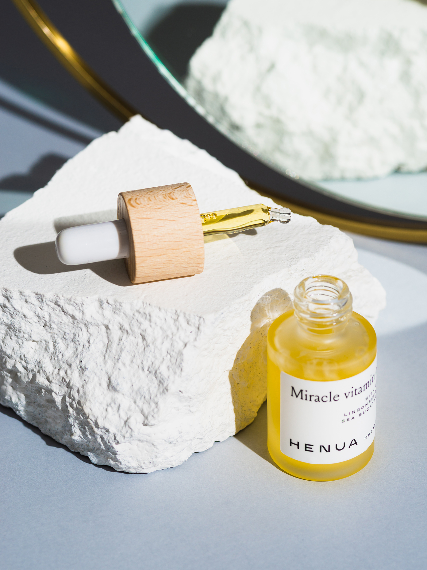 Henua Miracle Vitamin facial oil in a glass dropper bottle with wooden cap, displayed on a white textured stone.