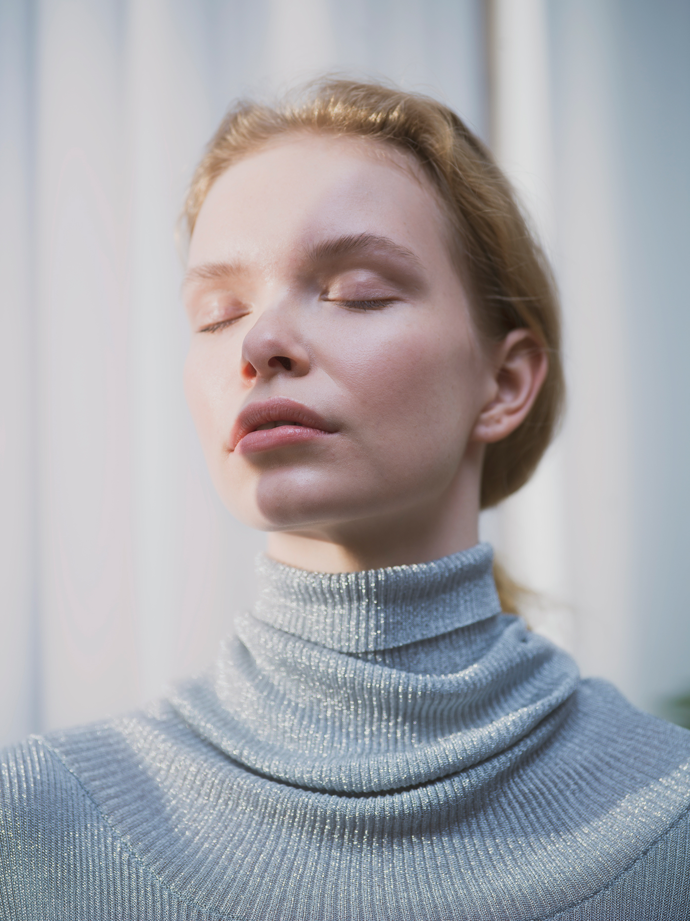 Close-up portrait of a model with closed eyes wearing a silver ribbed turtleneck sweater, shot for Henua by Werklig.