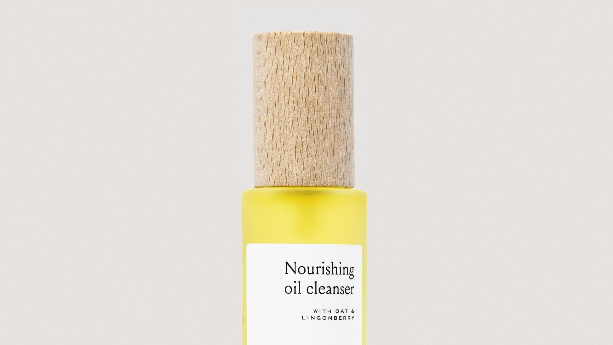 Henua Nourishing Oil Cleanser in a yellow frosted glass bottle with a cylindrical wooden cap.