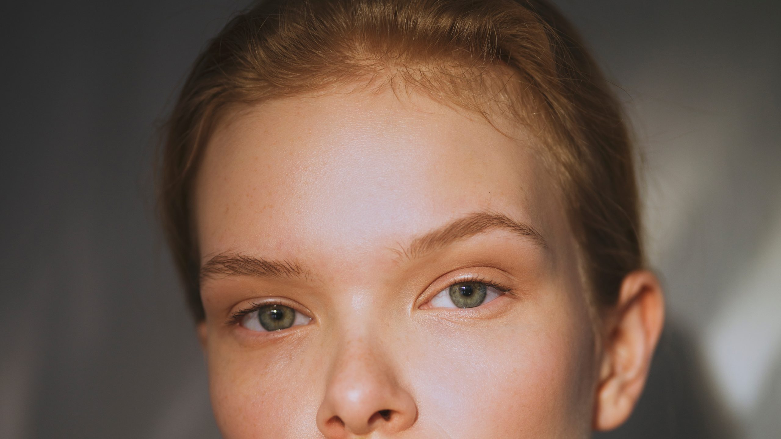 Close-up portrait of a young person with green eyes and short blonde hair, natural light, minimal aesthetic for Henua branding.