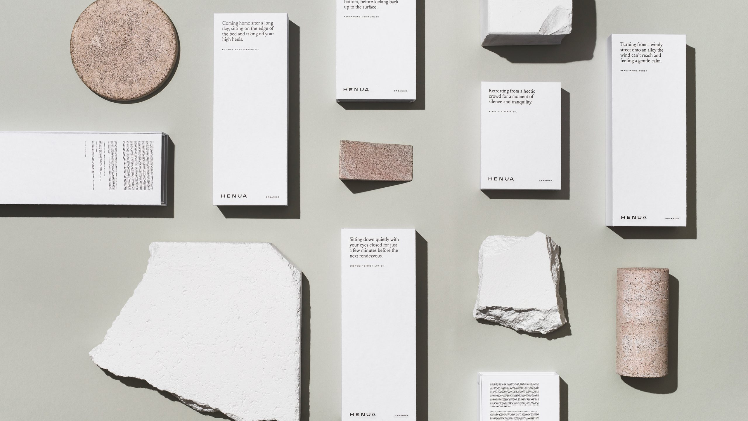 Henua Organics product packaging flatlay with white boxes, branded text, and natural stone and granite props on grey.
