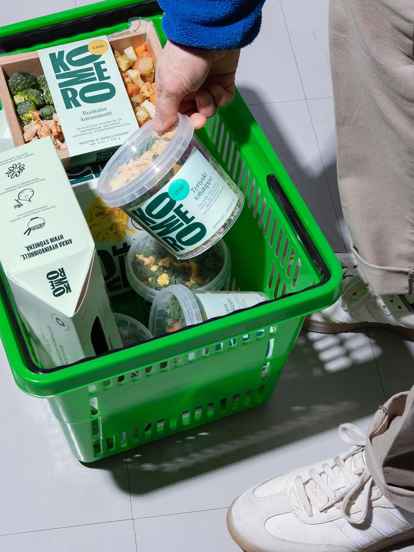 Hand placing a Komero product into a bright green shopping basket.
