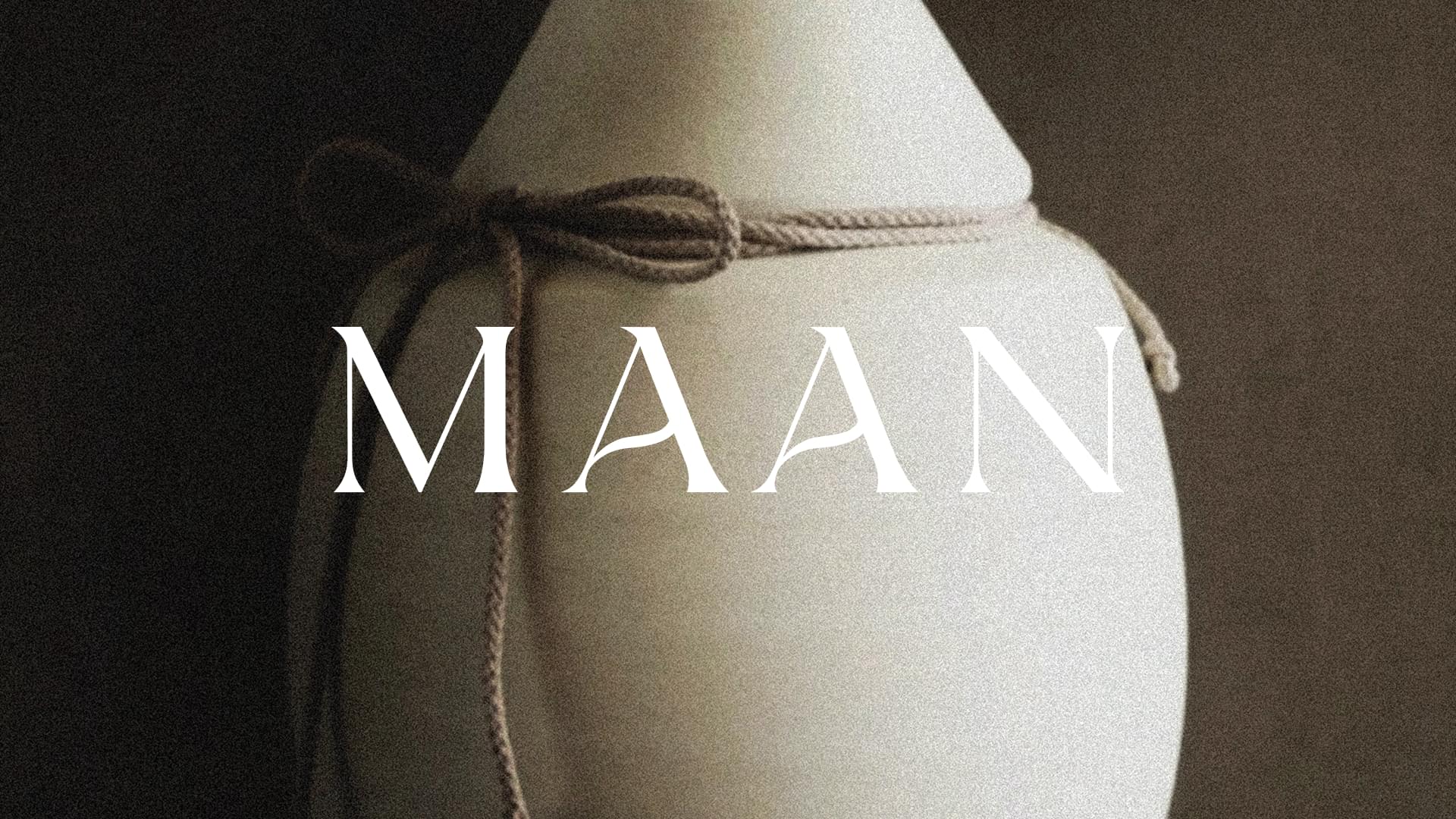 MAAN brand logo overlaid on a close-up of a cream ceramic vessel tied with natural twine rope.